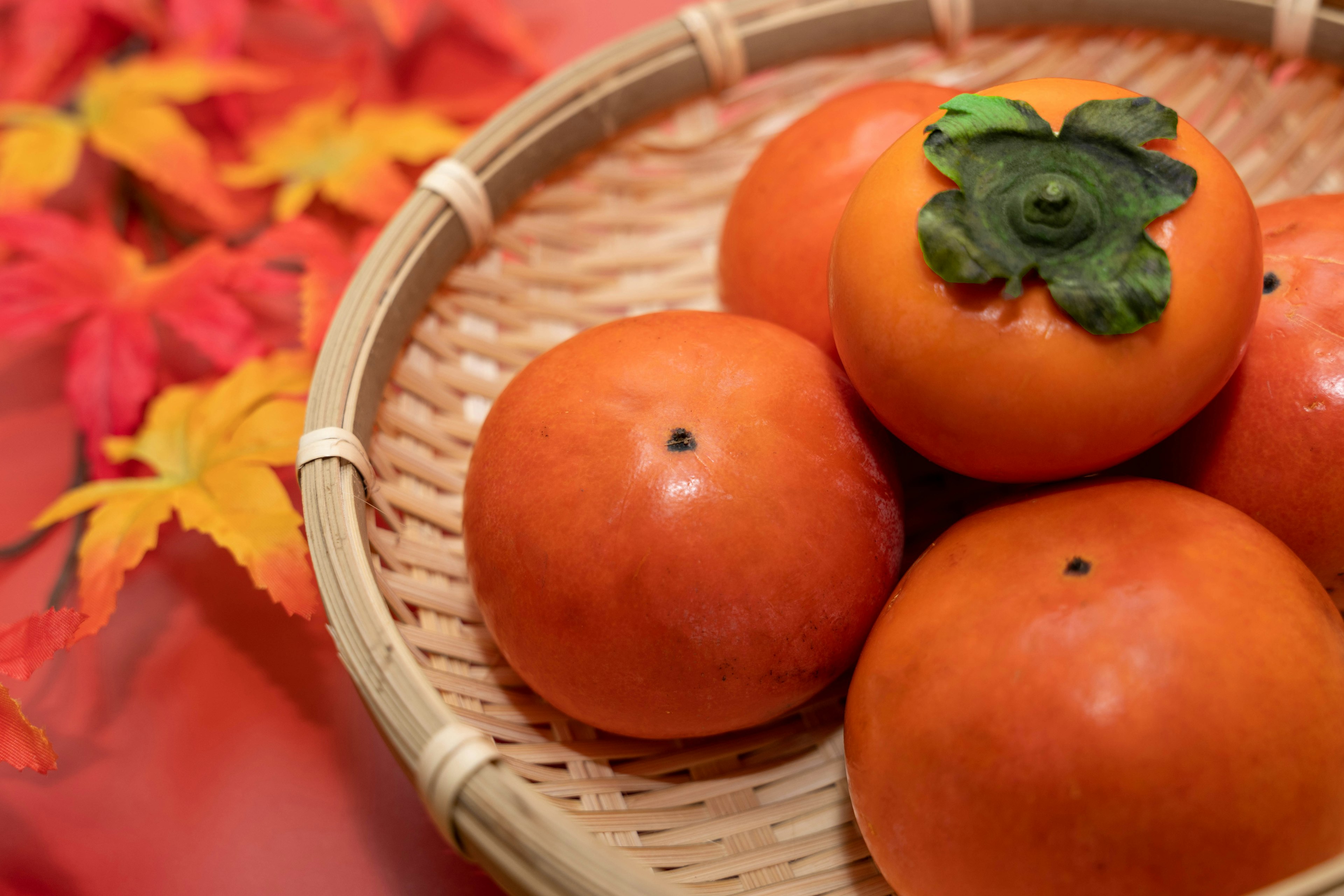 Kakis in einem geflochtenen Korb mit Herbstblättern