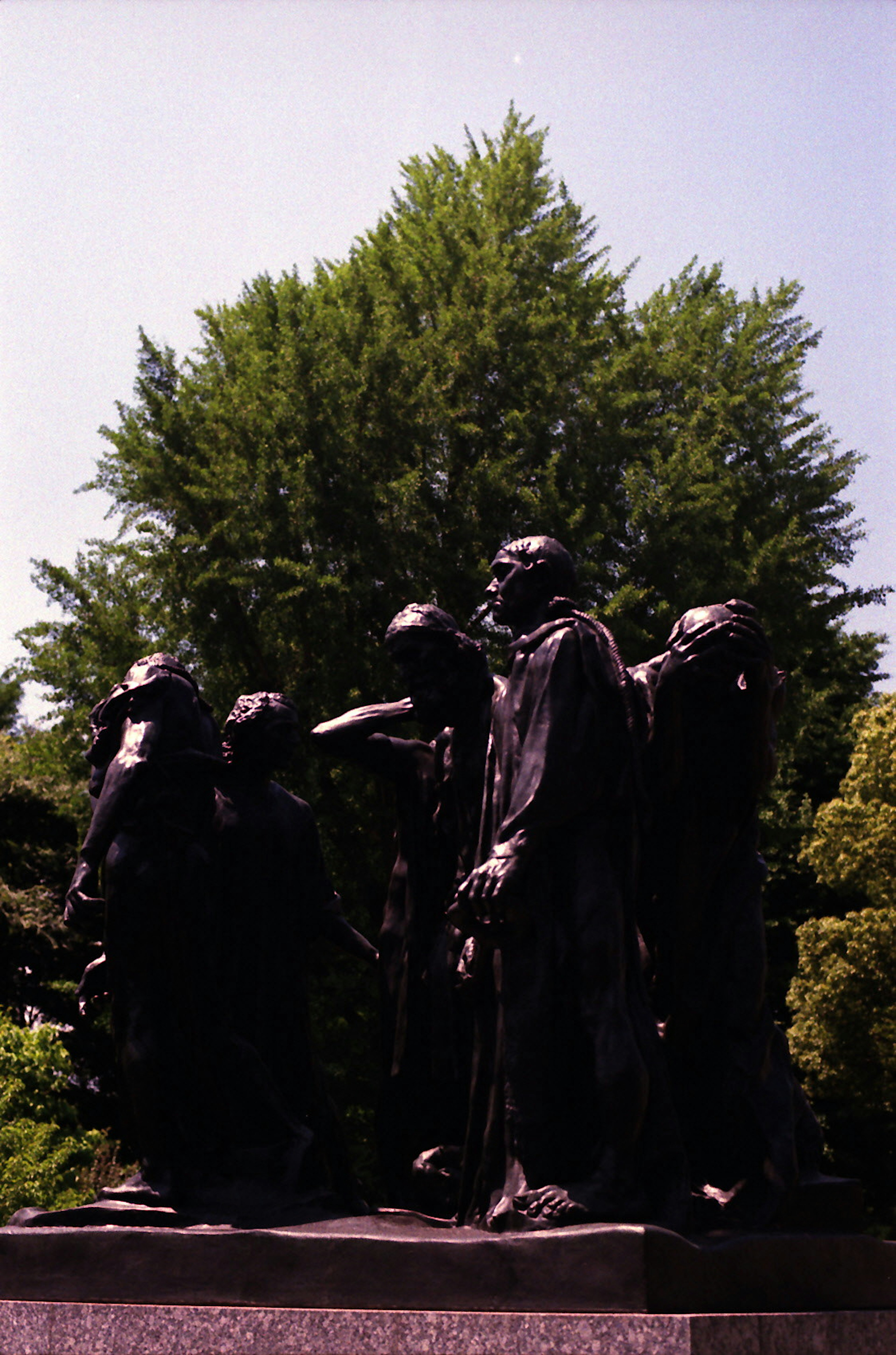 Eine Gruppe von Bronzekunstwerken, die unter einem blauen Himmel mit grünen Bäumen im Hintergrund stehen