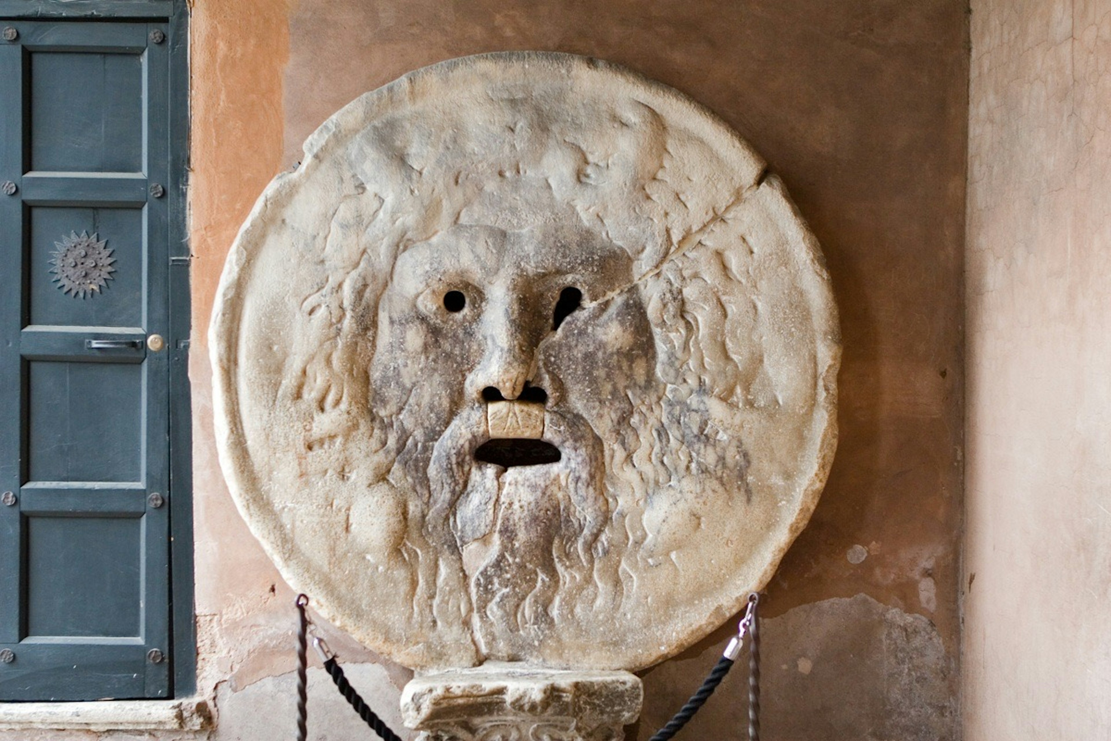 Antike Steinskulptur eines Gesichts mit offenem Mund an einer Wand montiert