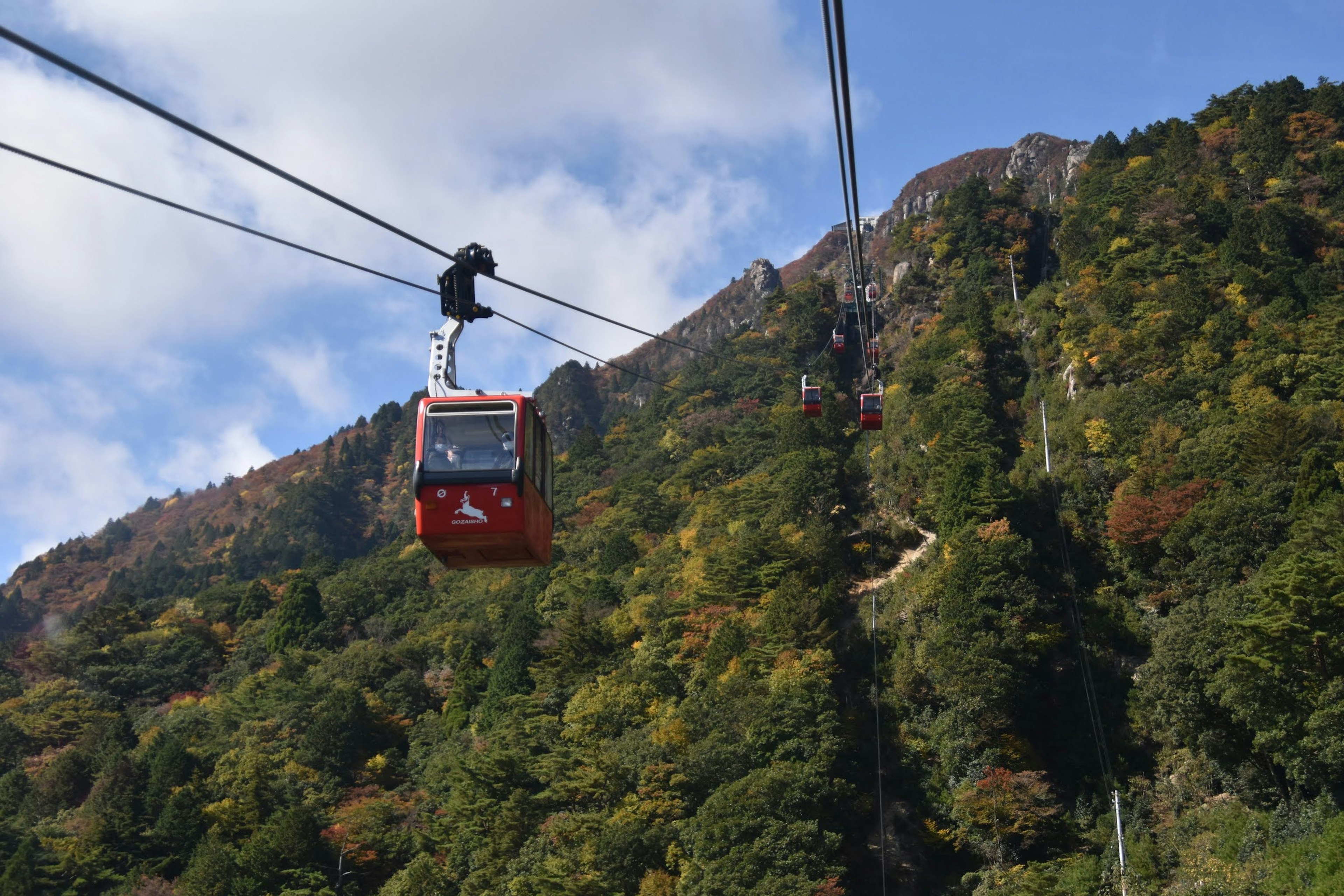 Teleférico rojo viajando por un costado de la montaña con follaje otoñal colorido