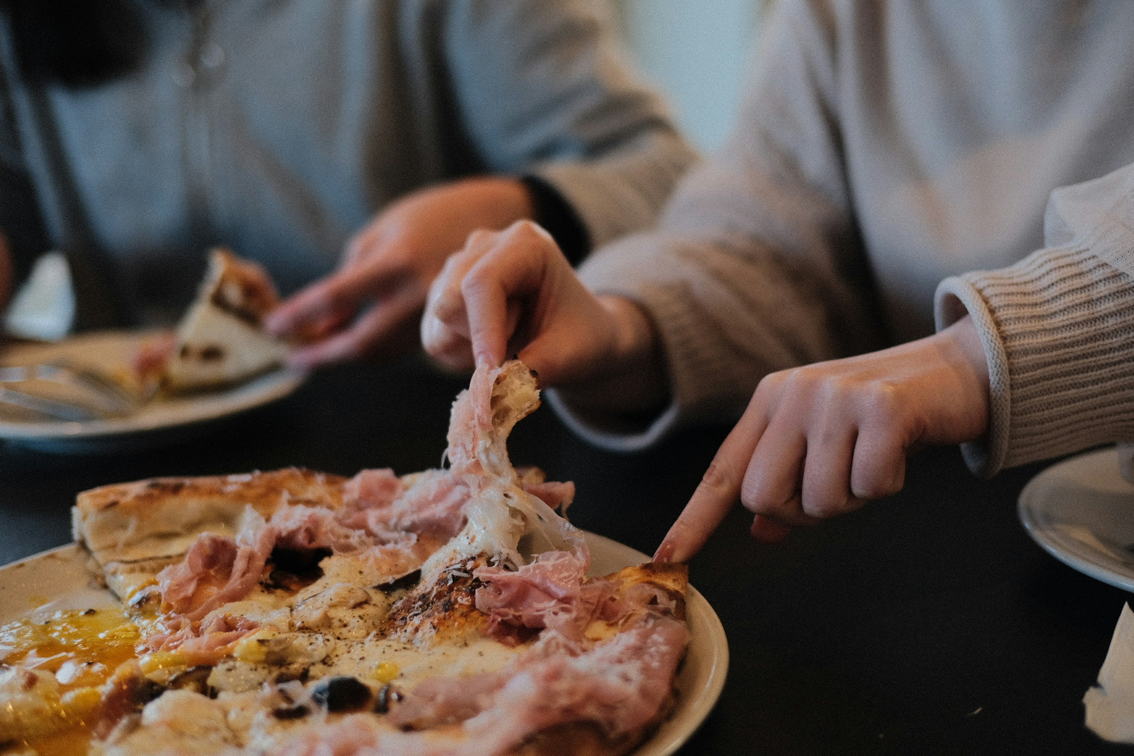 Primo piano di due mani che condividono una fetta di pizza su un tavolo con condimenti visibili