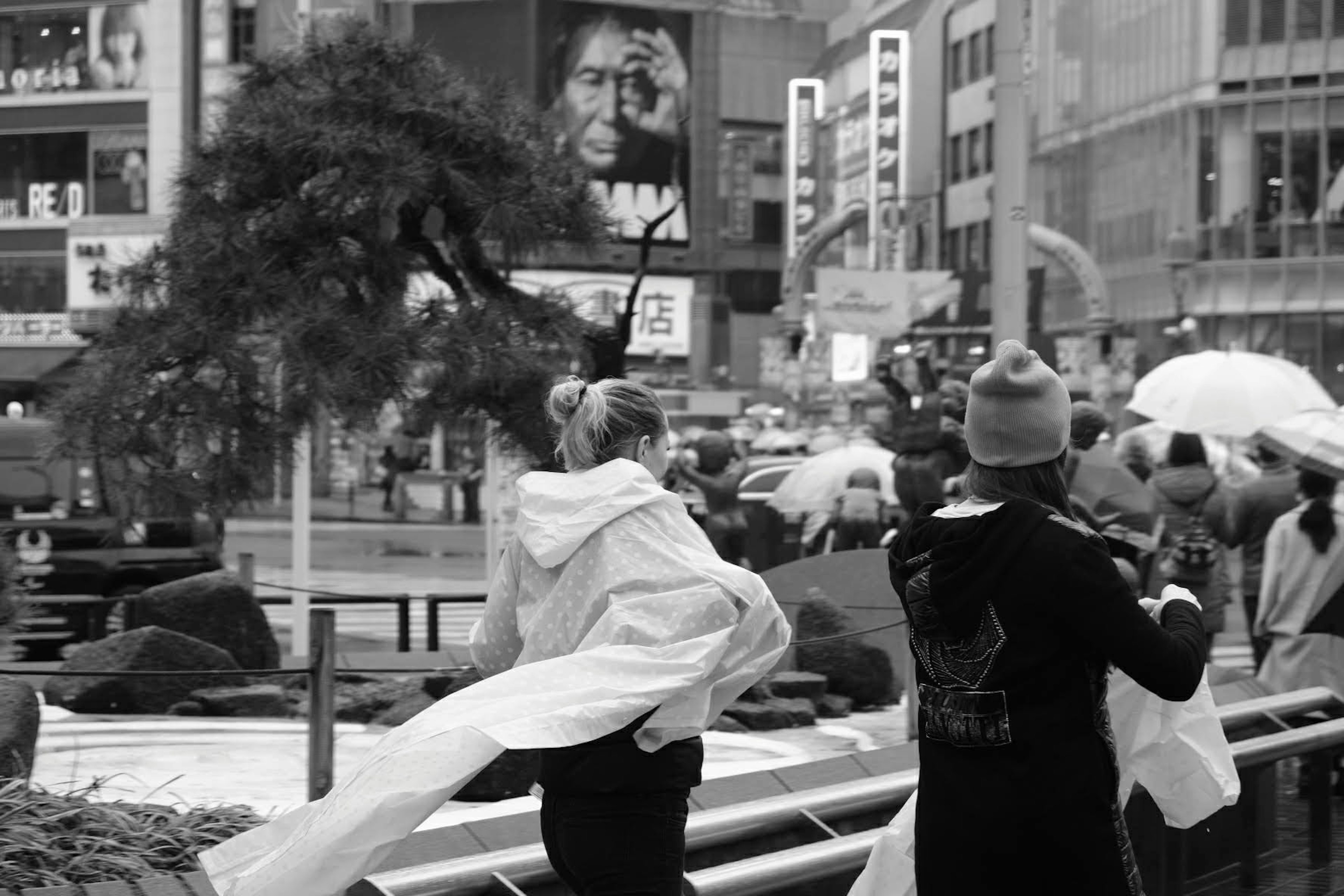 Escena de ciudad con personas sosteniendo paraguas y una mujer con una tela blanca bajo la lluvia