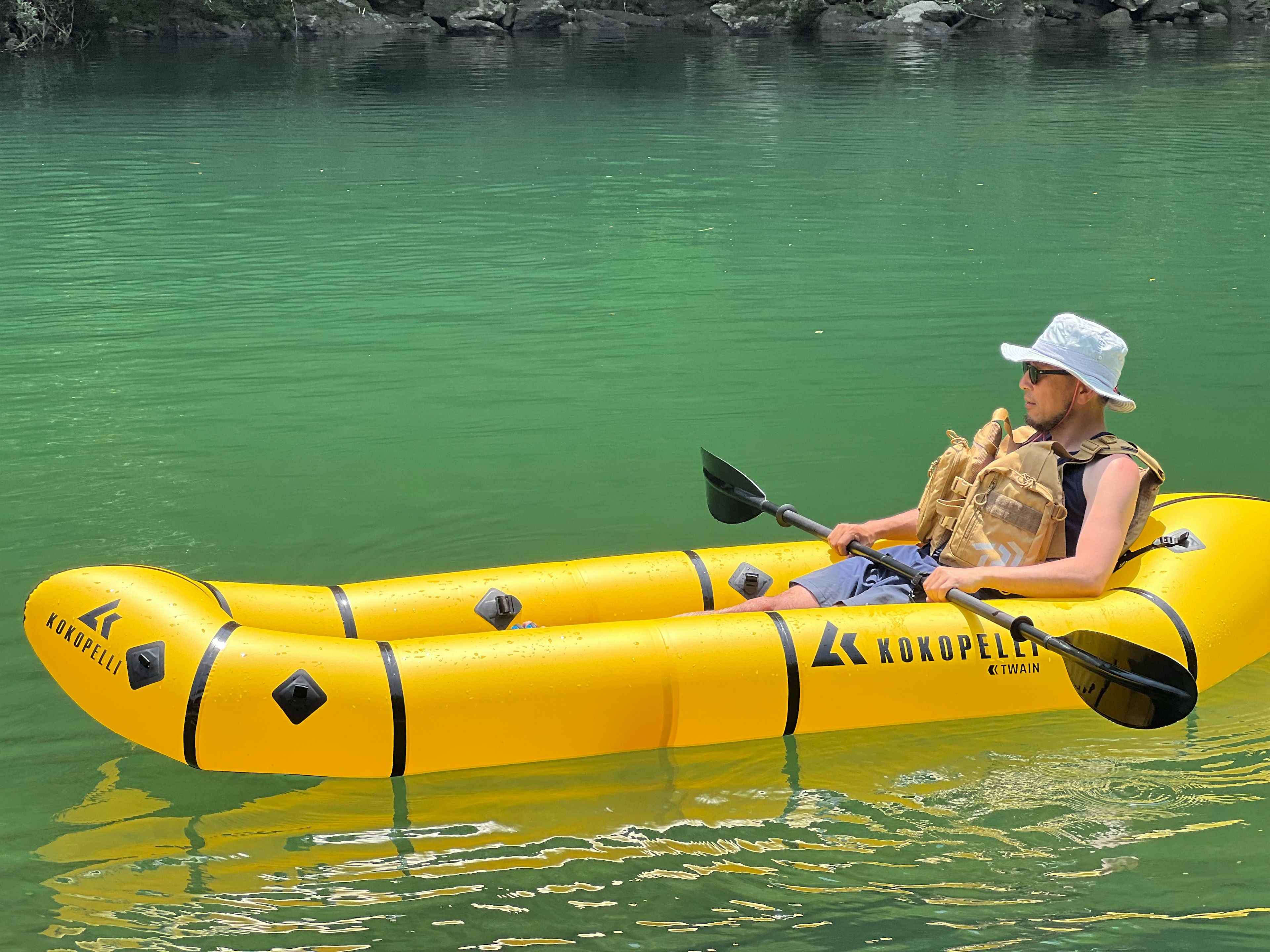 A man kayaking in a bright yellow inflatable kayak on green water