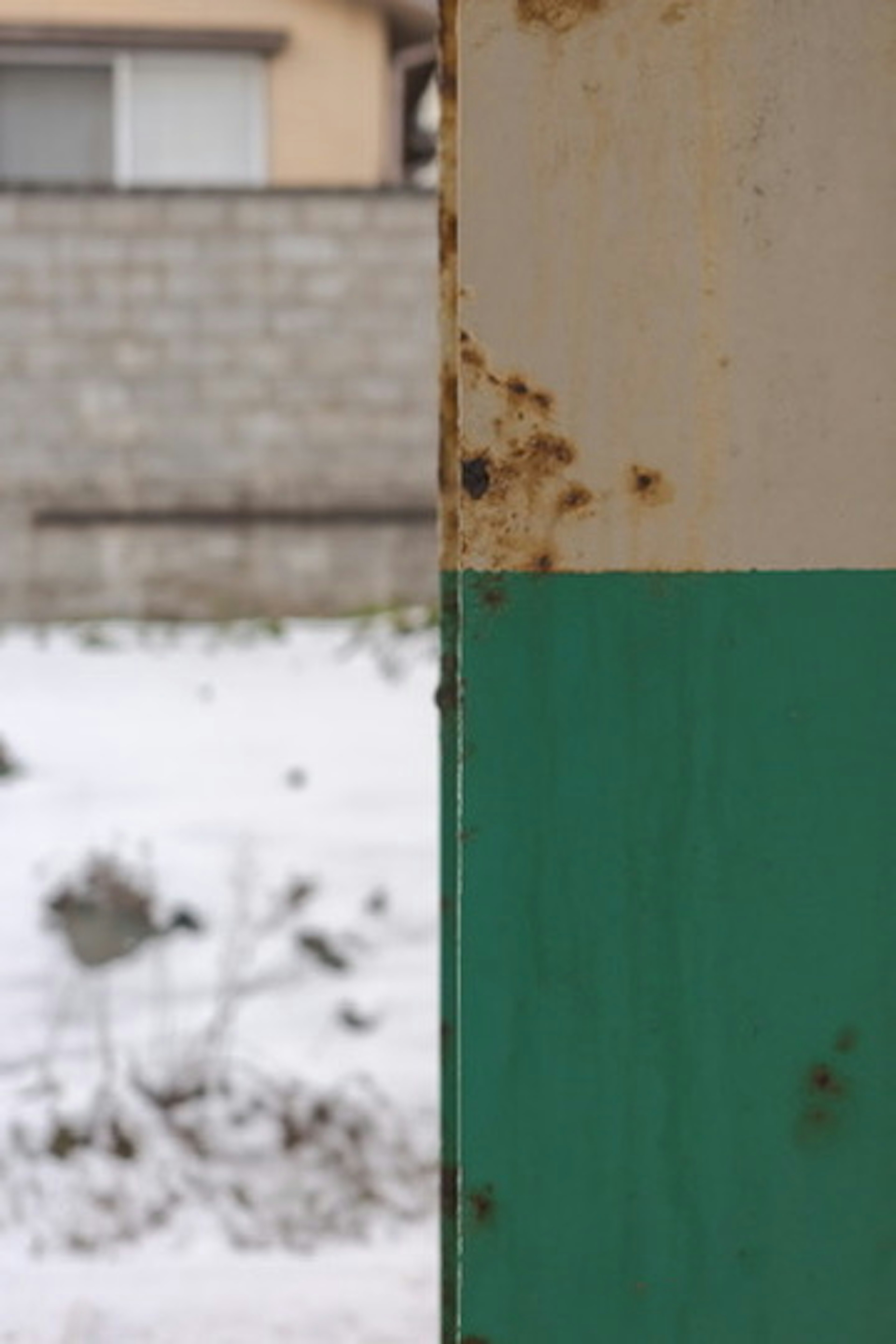 Rusty metal edge with green and white paint snow-covered ground in the background