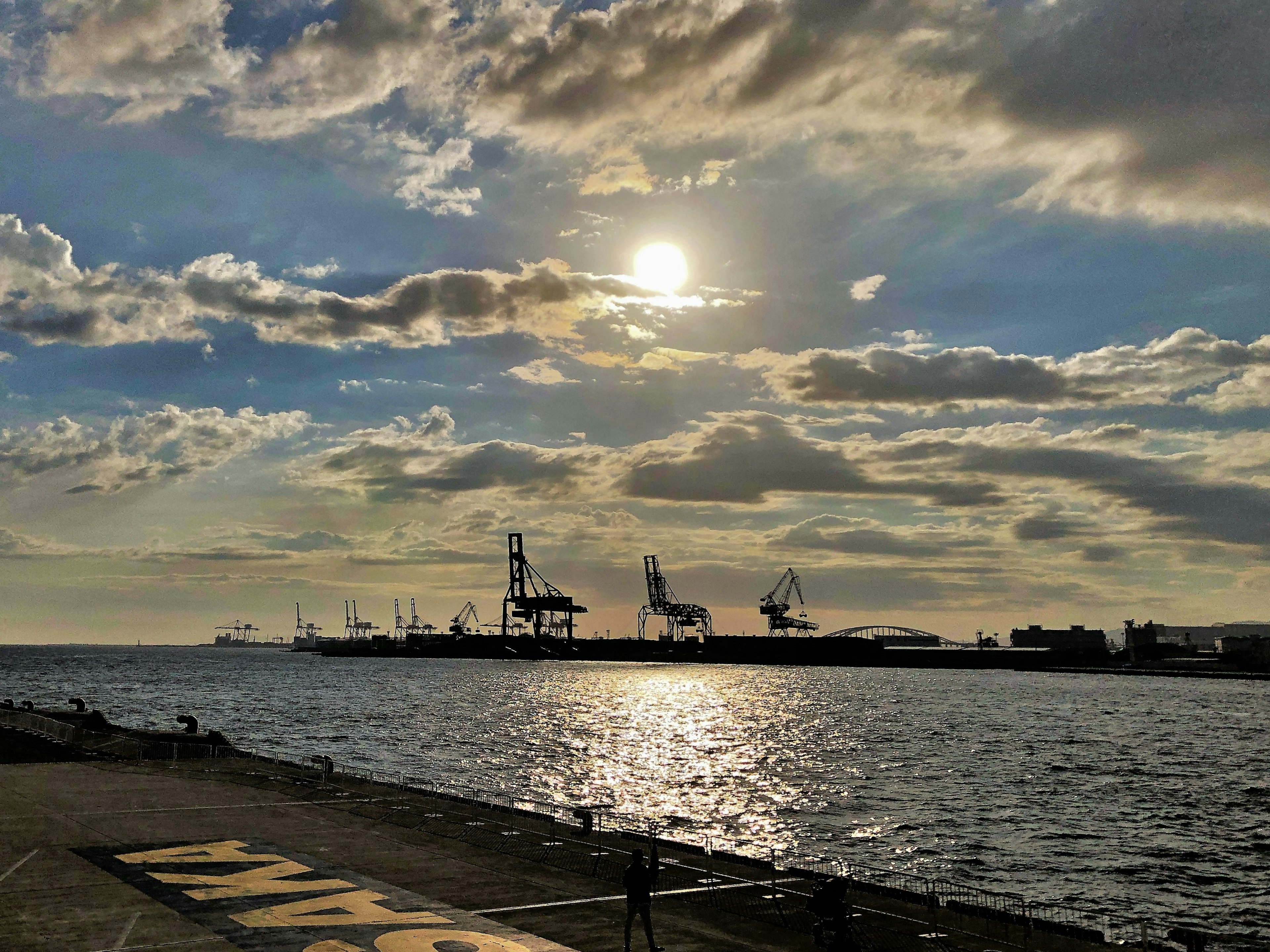 Hafenansicht mit Sonne, die sich auf dem Wasser spiegelt und bewölkten Himmel