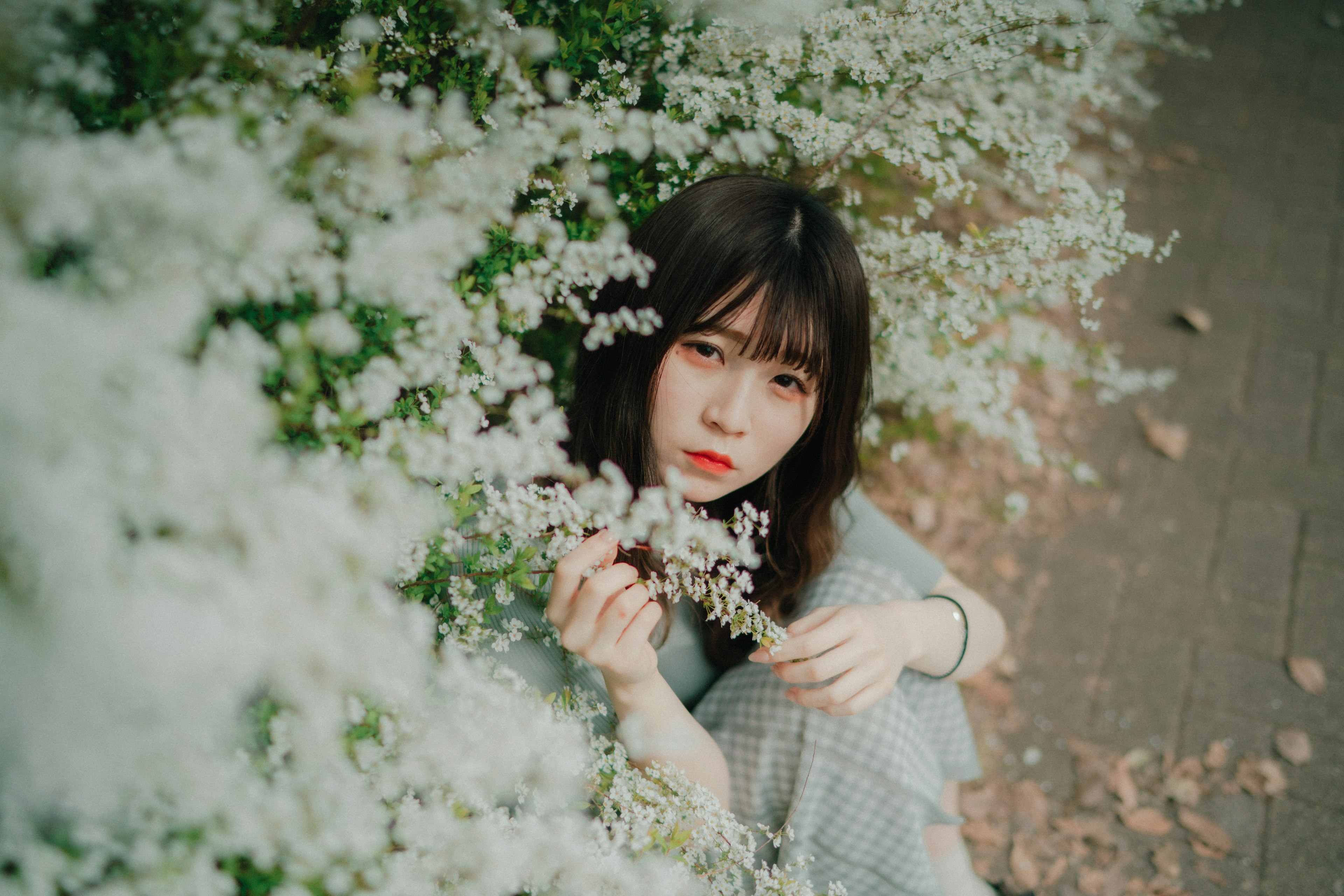 Portrait of a woman surrounded by white flowers she is holding a flower with a serene expression