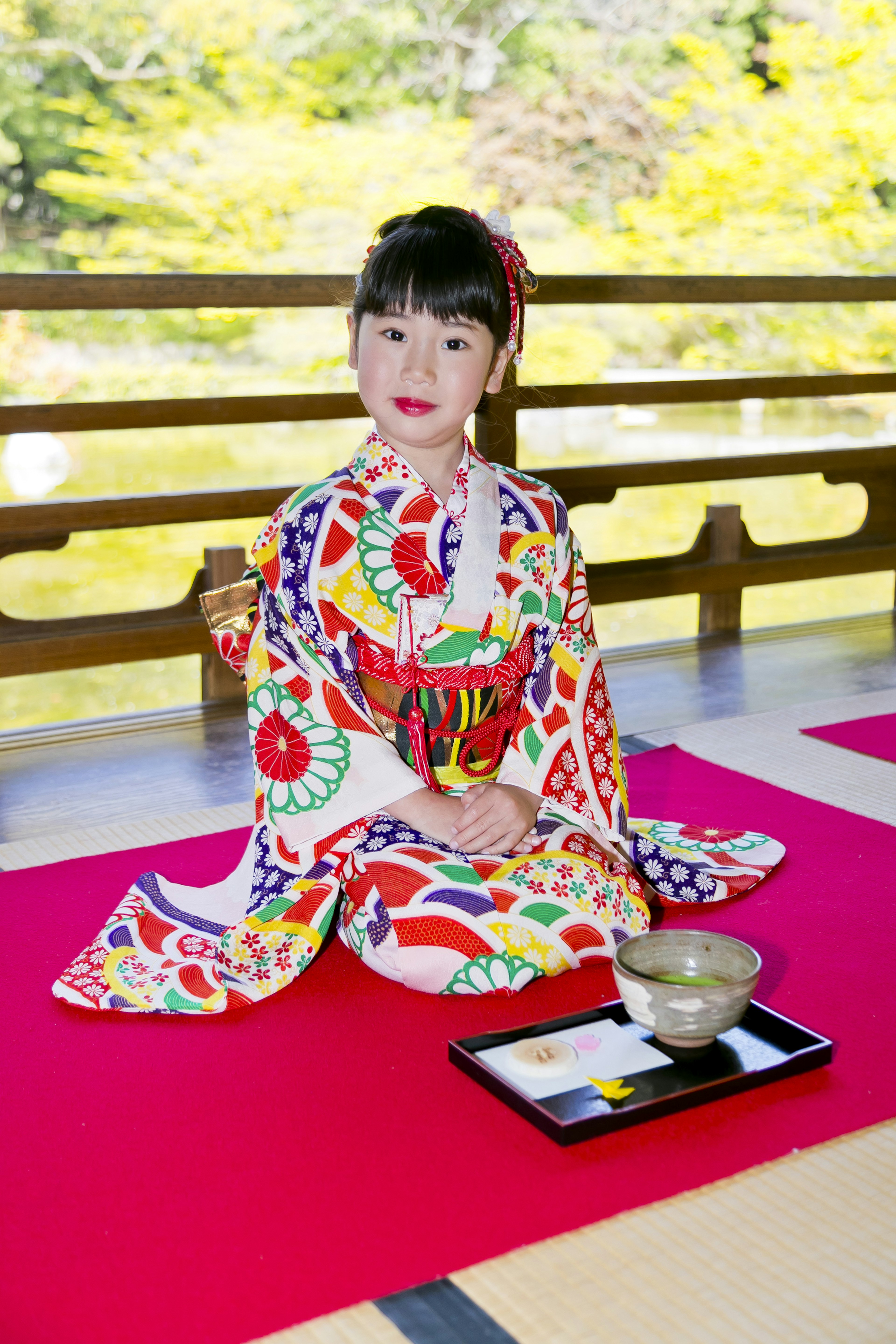 Una niña con un kimono colorido sentada en un hermoso jardín japonés preparando una ceremonia del té