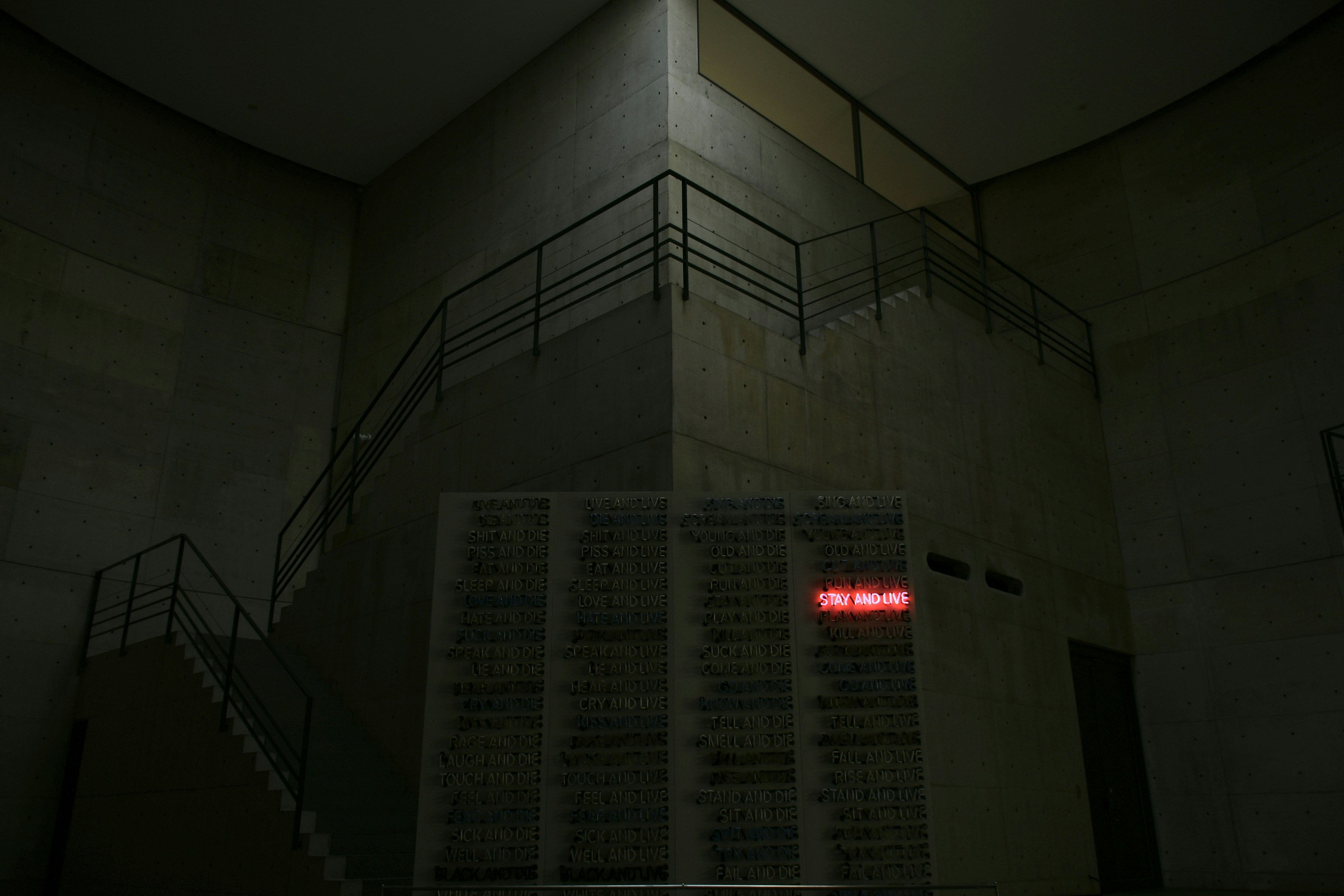 Dark stairwell with concrete walls featuring a prominent red illuminated sign