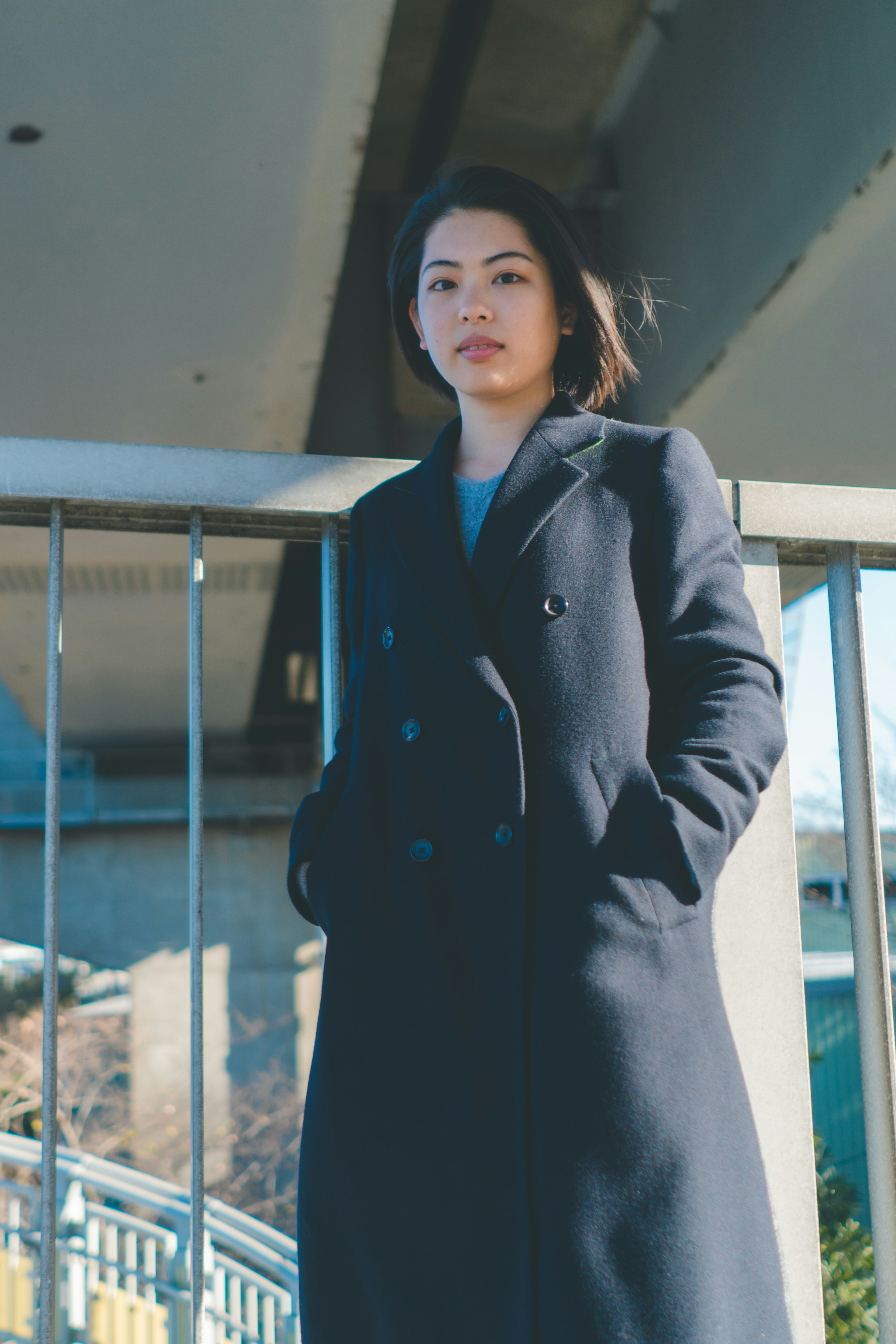 Woman in a black coat standing under a bridge