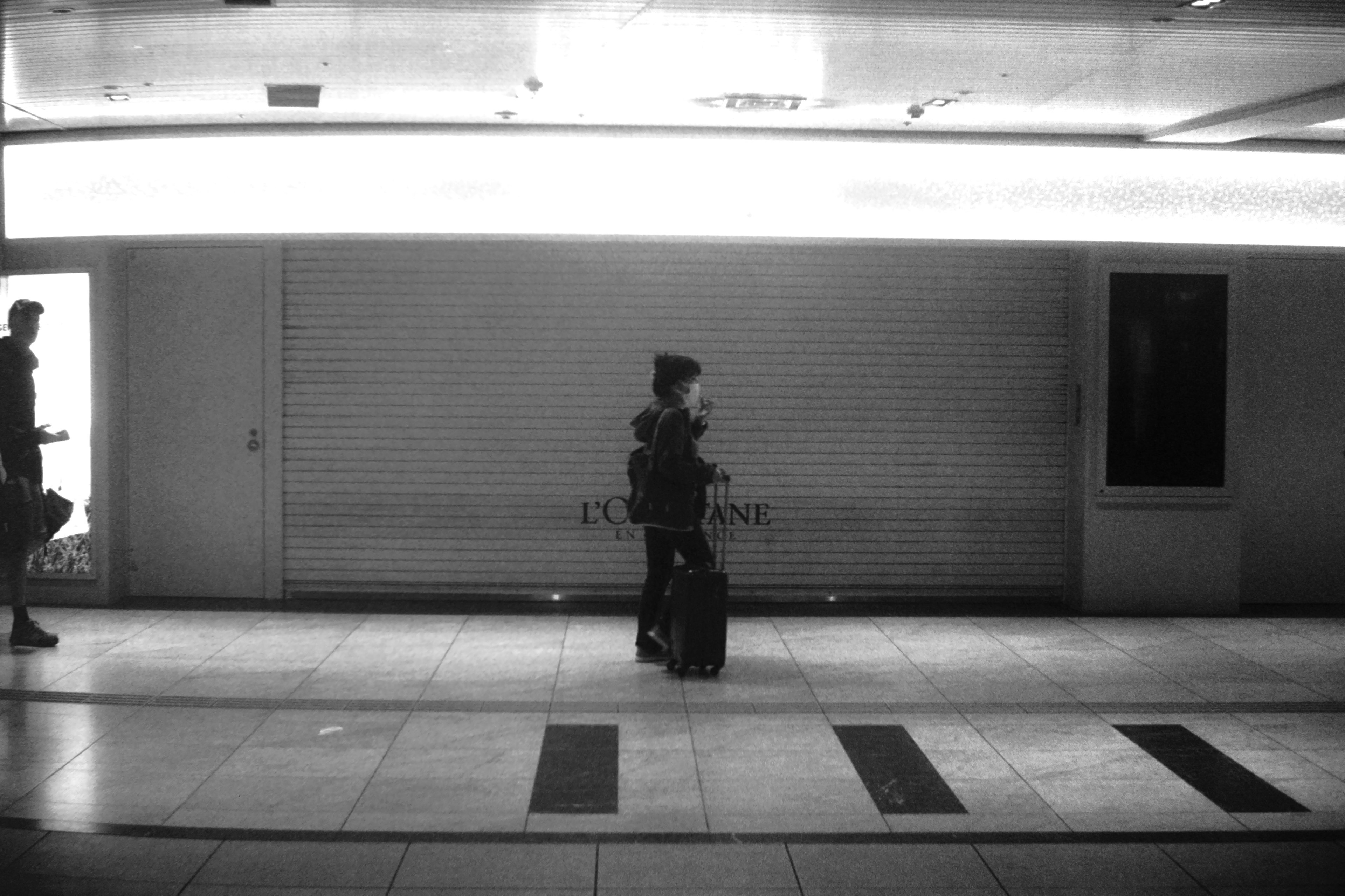 Un viajero caminando en un pasillo de estación débilmente iluminado frente a una tienda cerrada