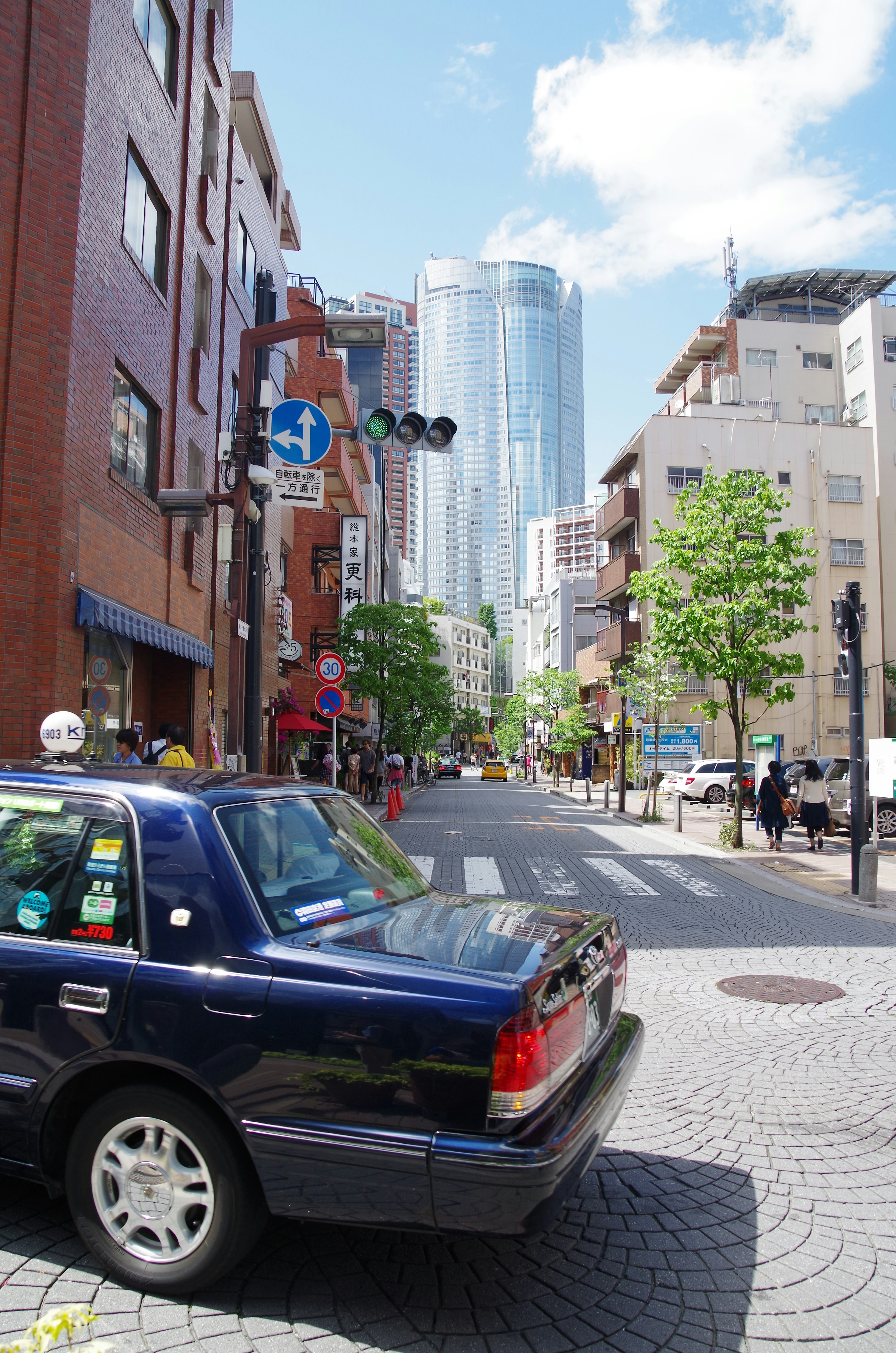 Blue taxi parked at a street corner with a skyscraper in the background