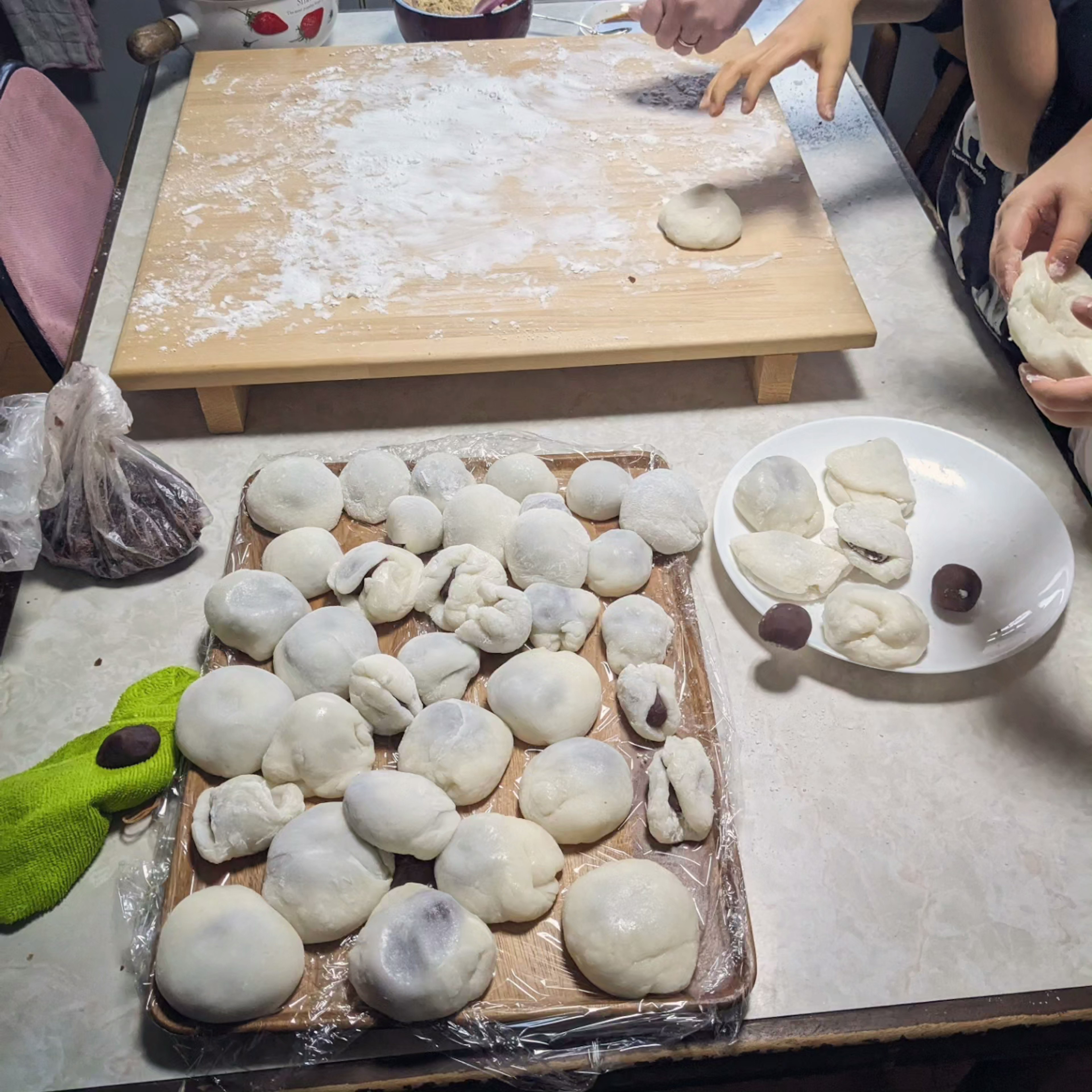 一张木桌上有许多白色饺子和撒了面粉的工作区域