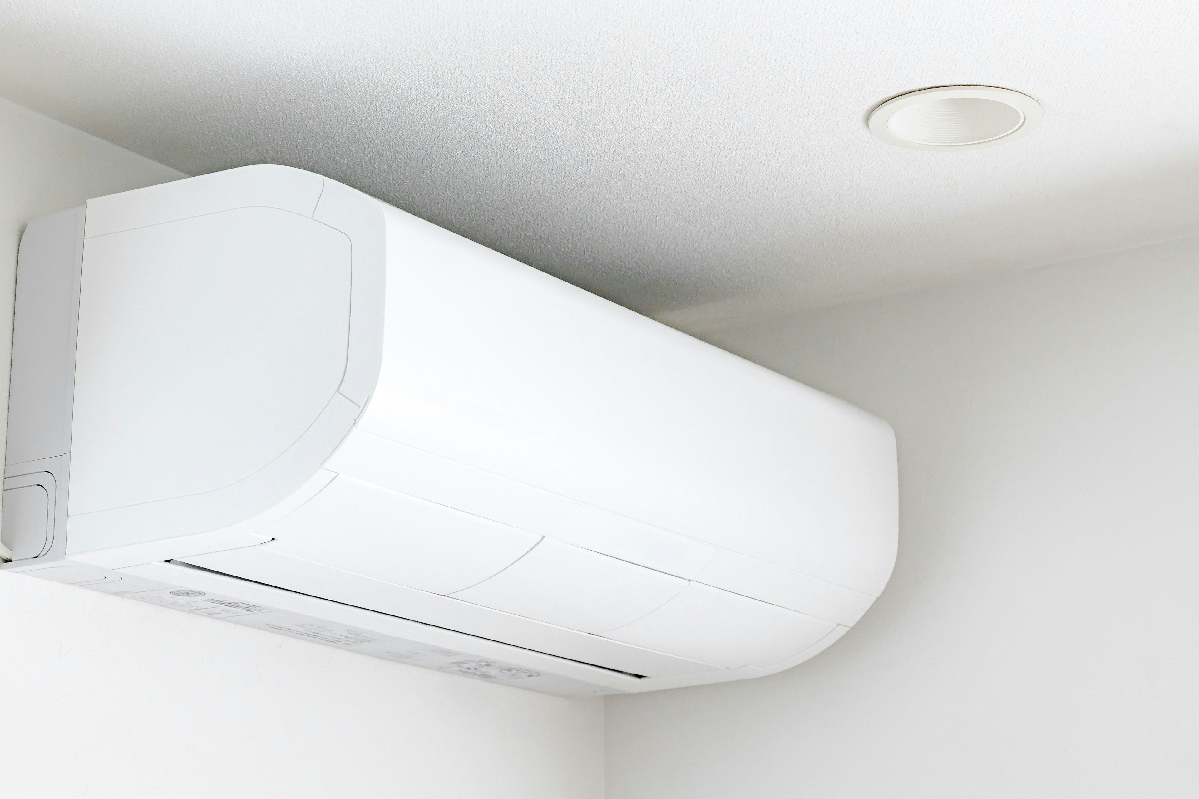 A white air conditioner mounted high on a wall in a simple indoor setting