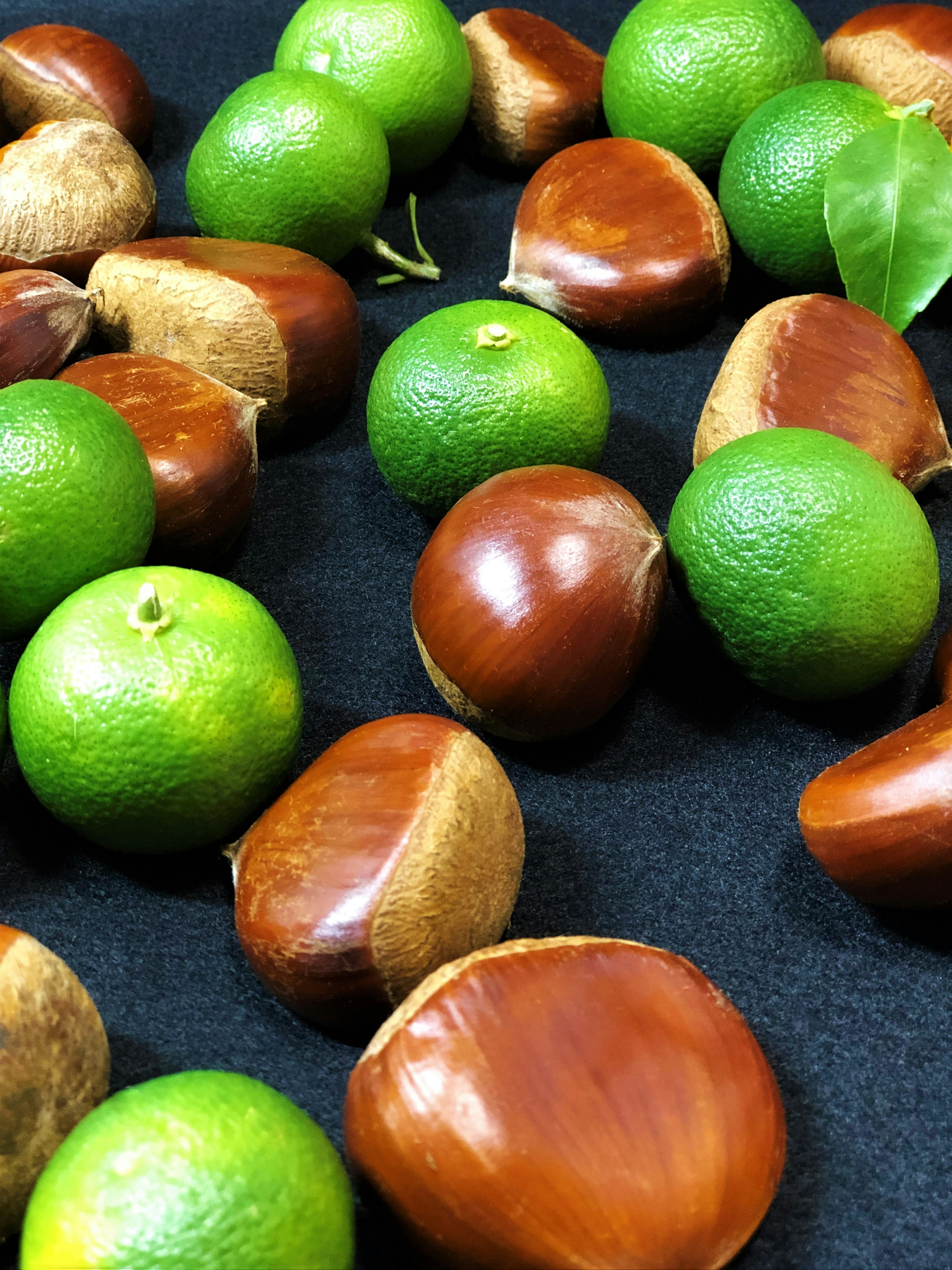 A mix of green limes and brown chestnuts on a dark surface