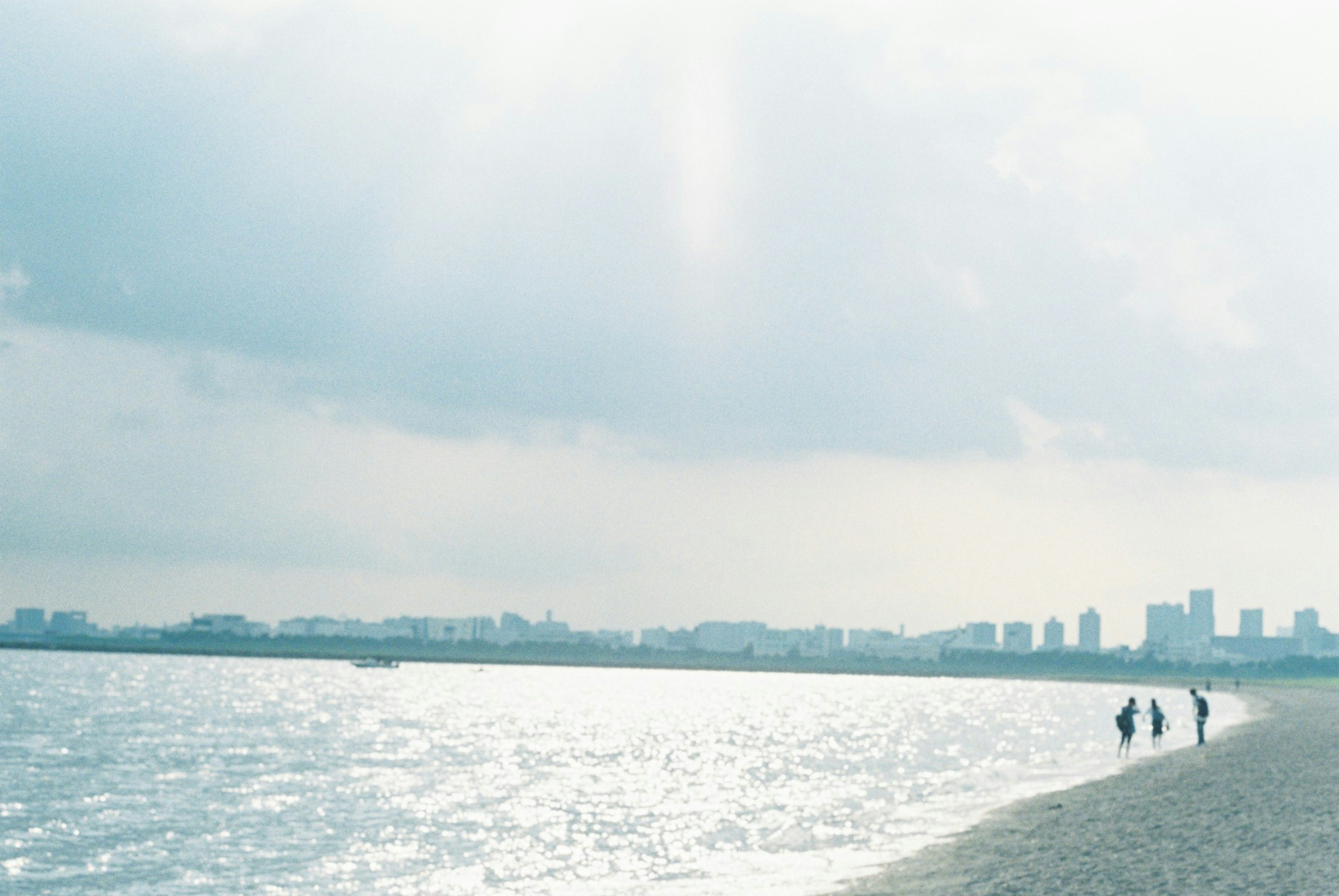 People walking along a tranquil beach with a city skyline in the background