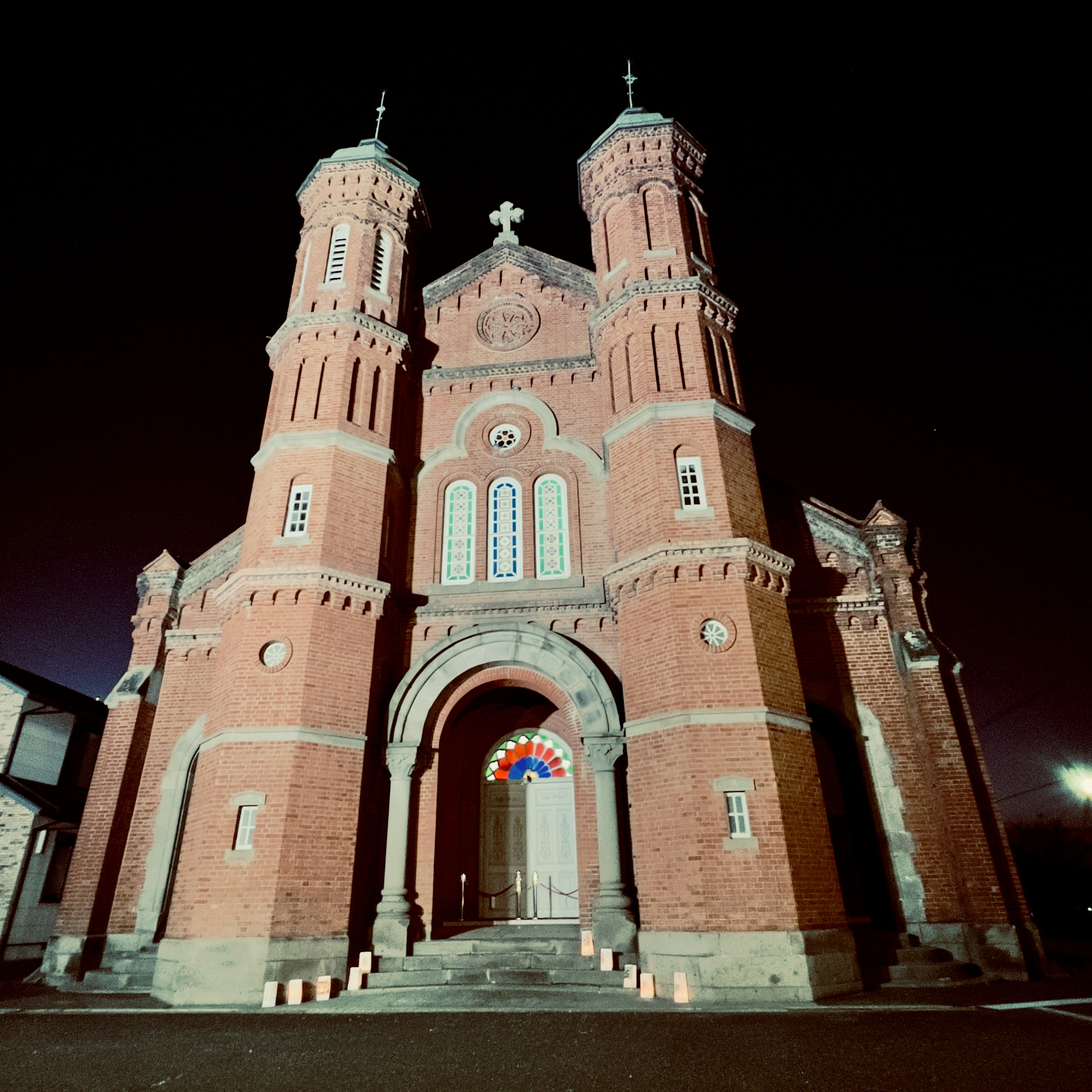 Vue nocturne d'une église en briques rouges avec deux tours et une entrée en arc