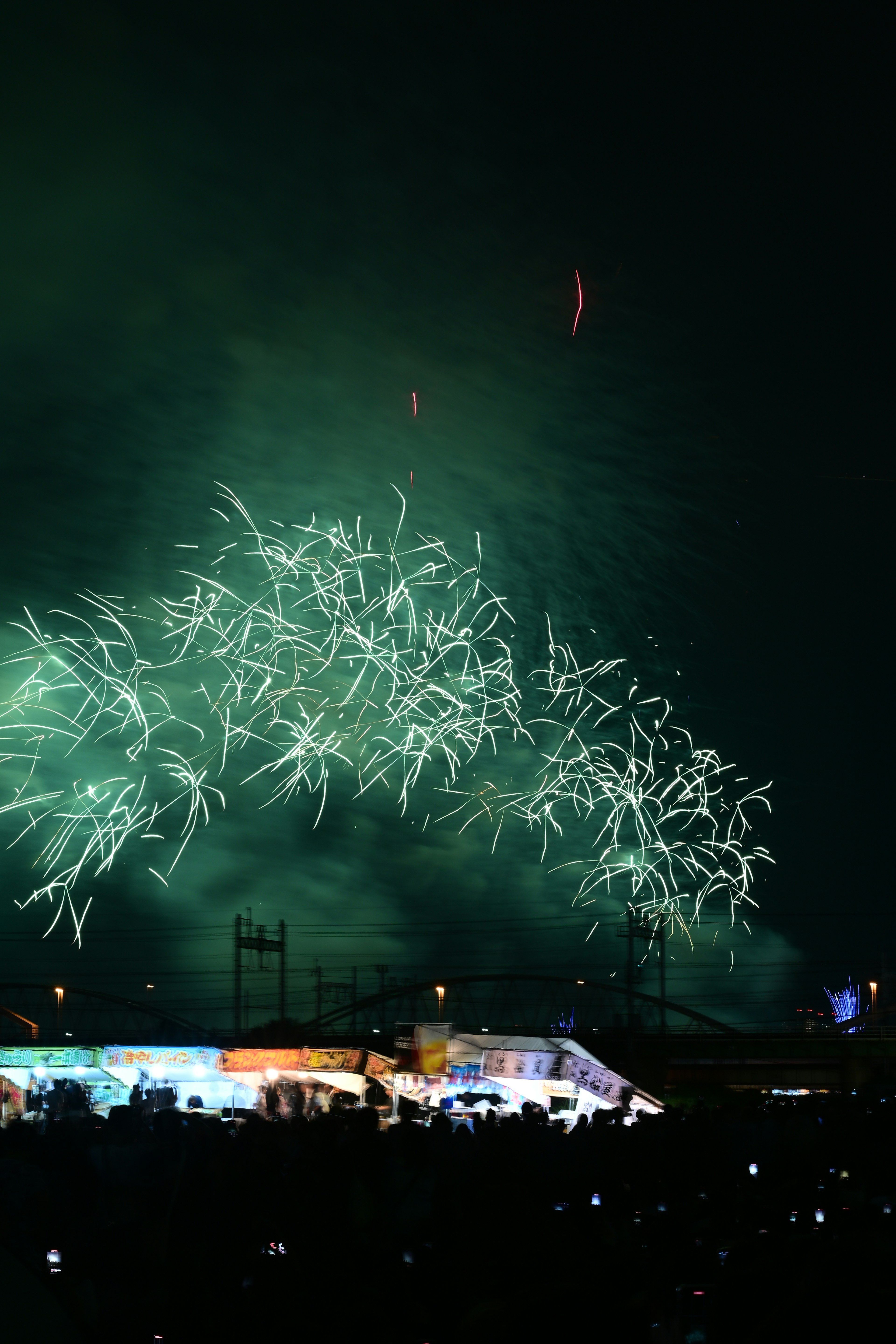 Green fireworks arching across the night sky with silhouettes of spectators