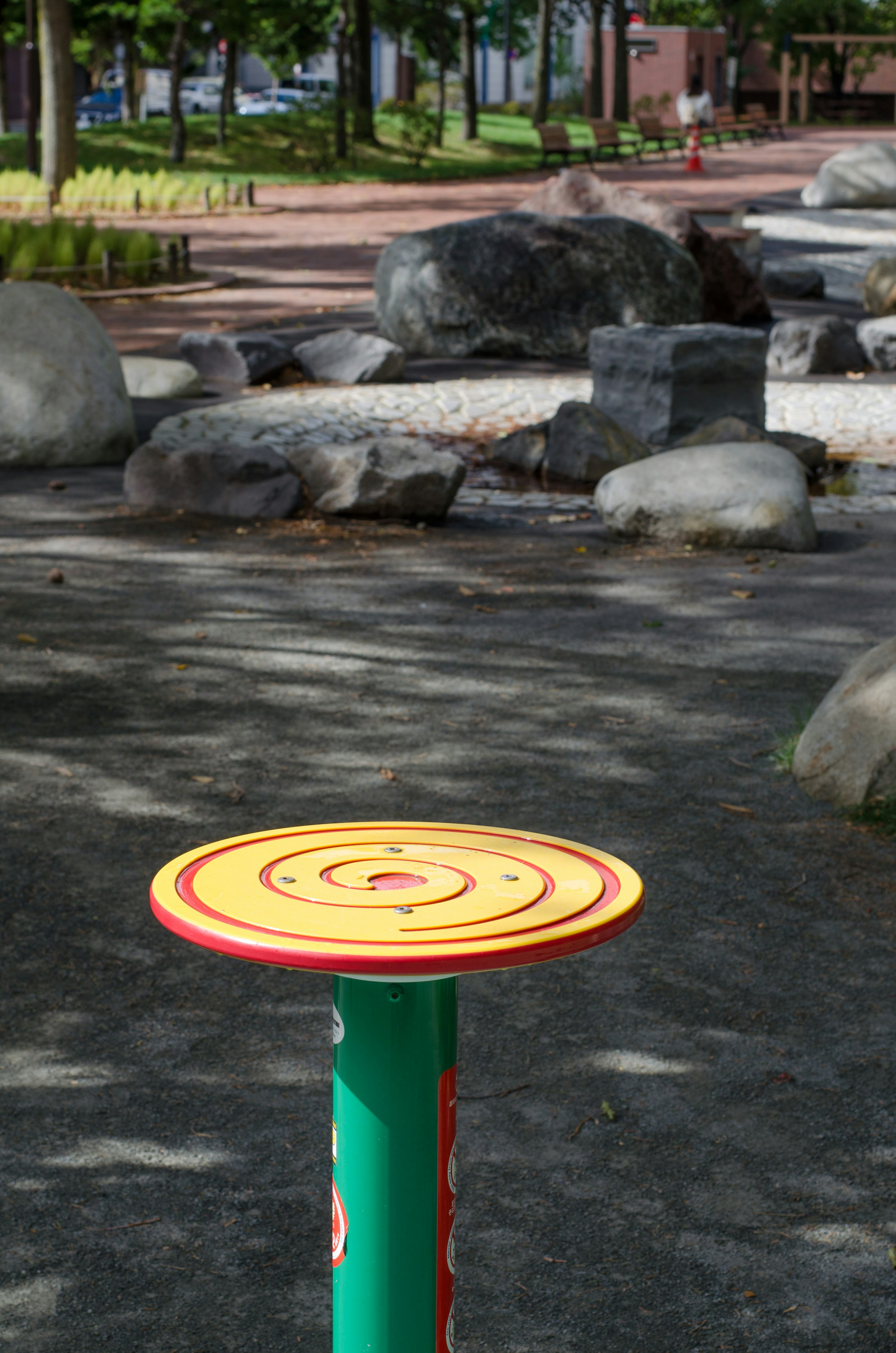 Plataforma circular amarilla sobre un poste verde en un parque con rocas grandes de fondo