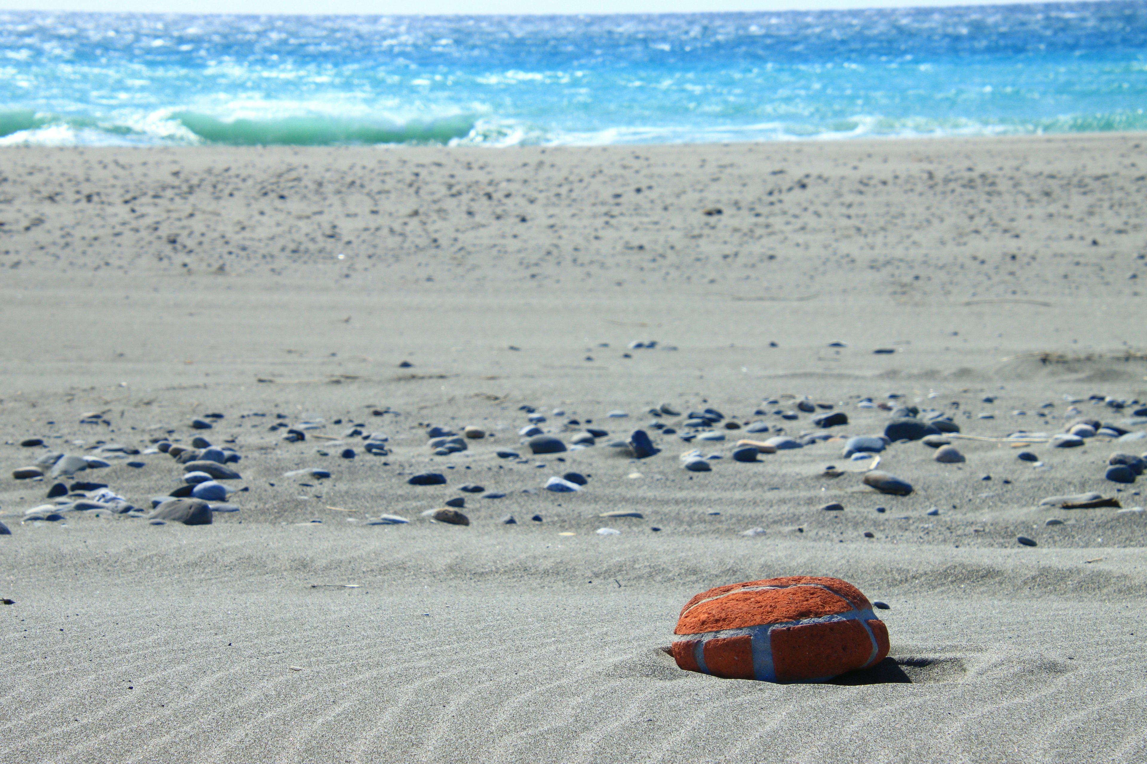 An orange life buoy on the sandy beach with a blue ocean in the background