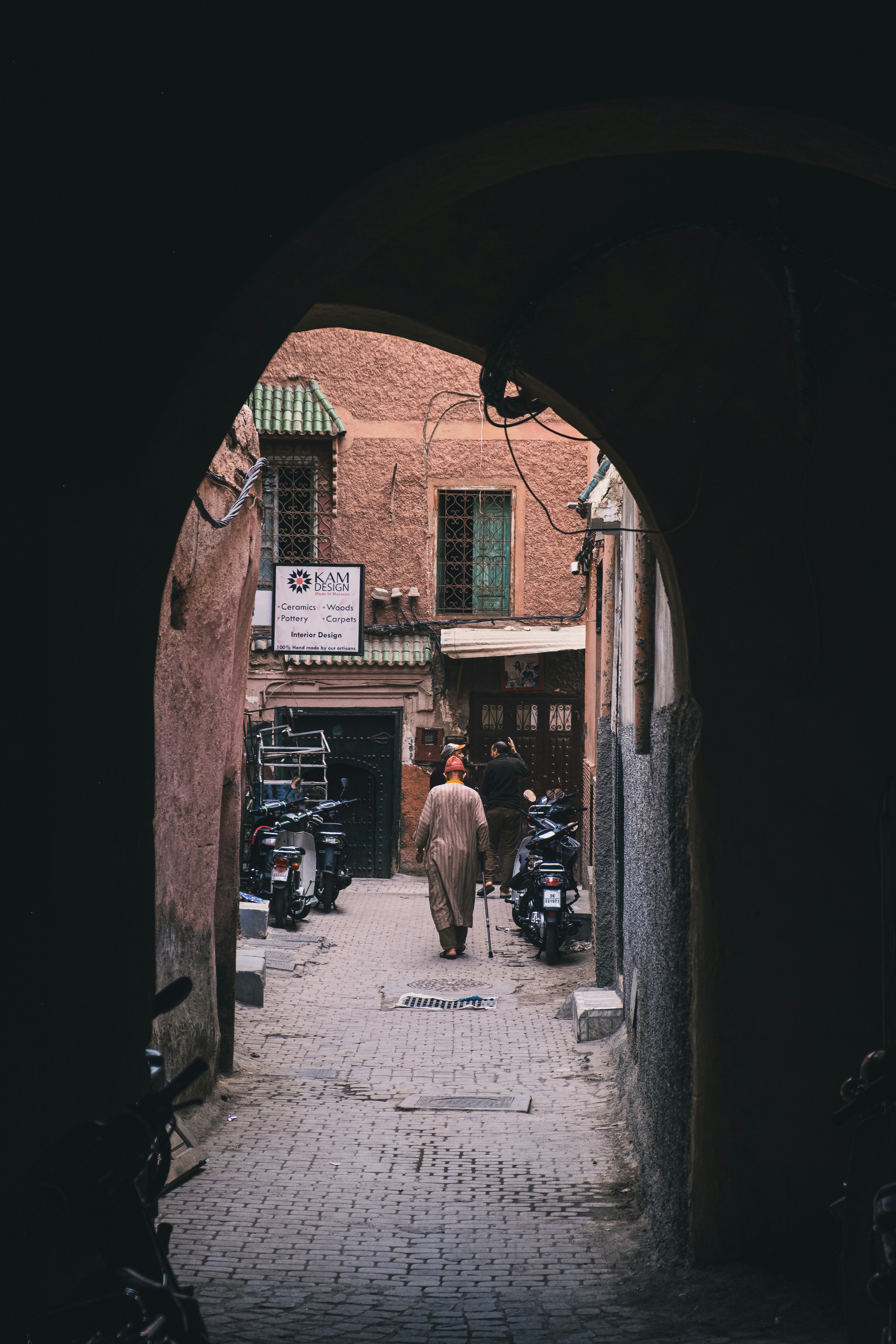 A person walking through an archway with reddish buildings in the background