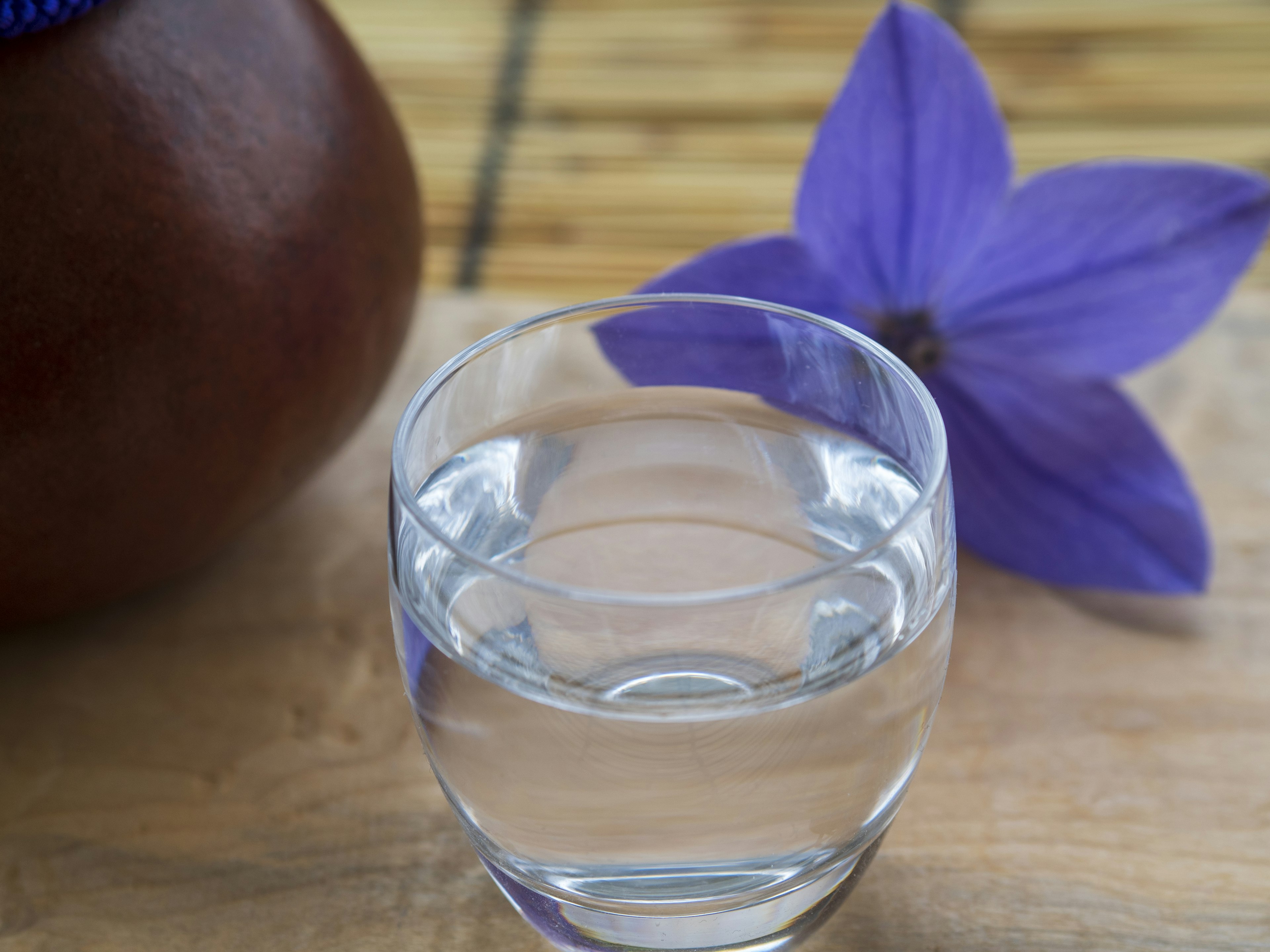 Imagen con un vaso de agua clara y una flor morada