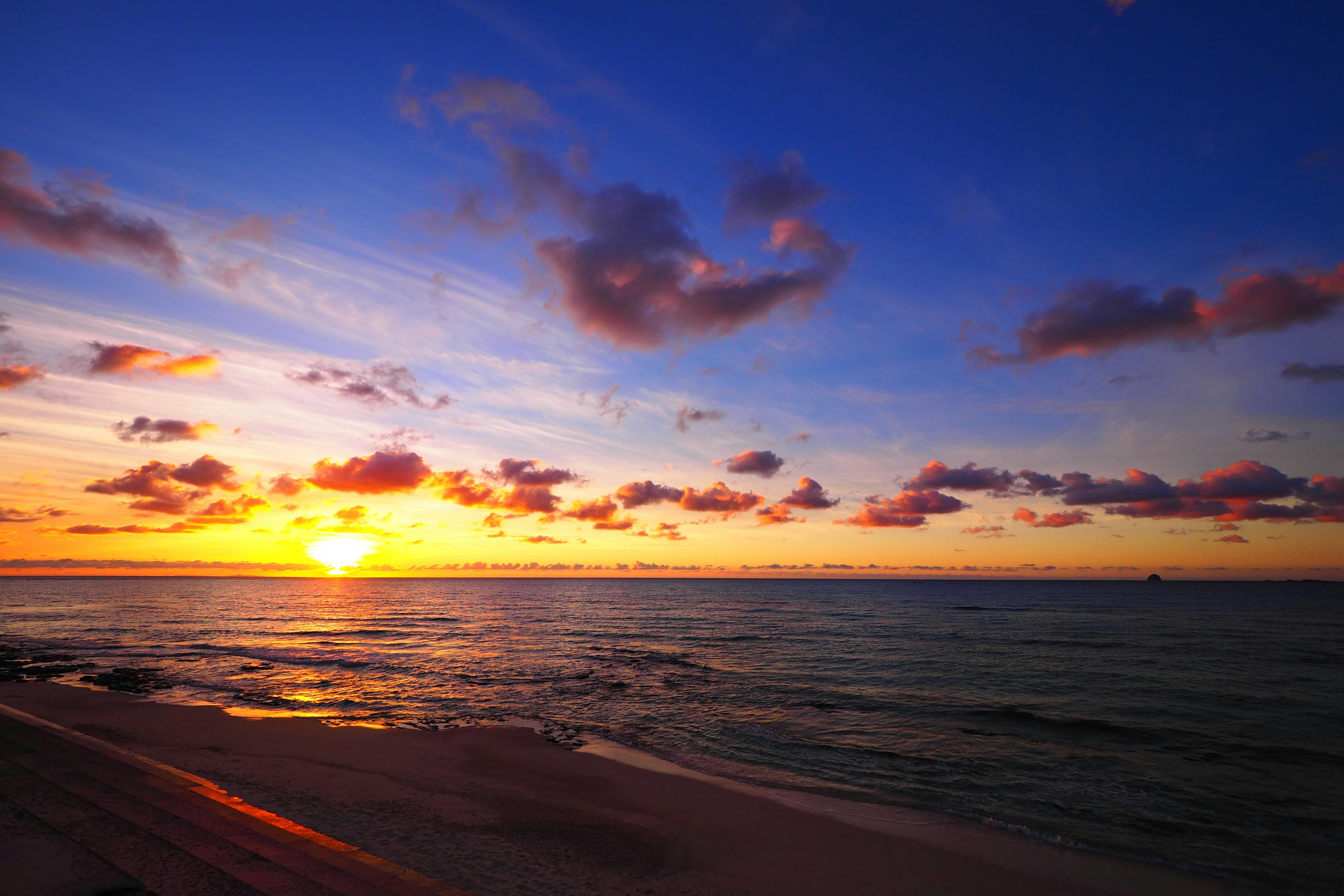 Splendido tramonto sull'oceano con sole arancione che affonda nell'acqua e cielo blu con nuvole