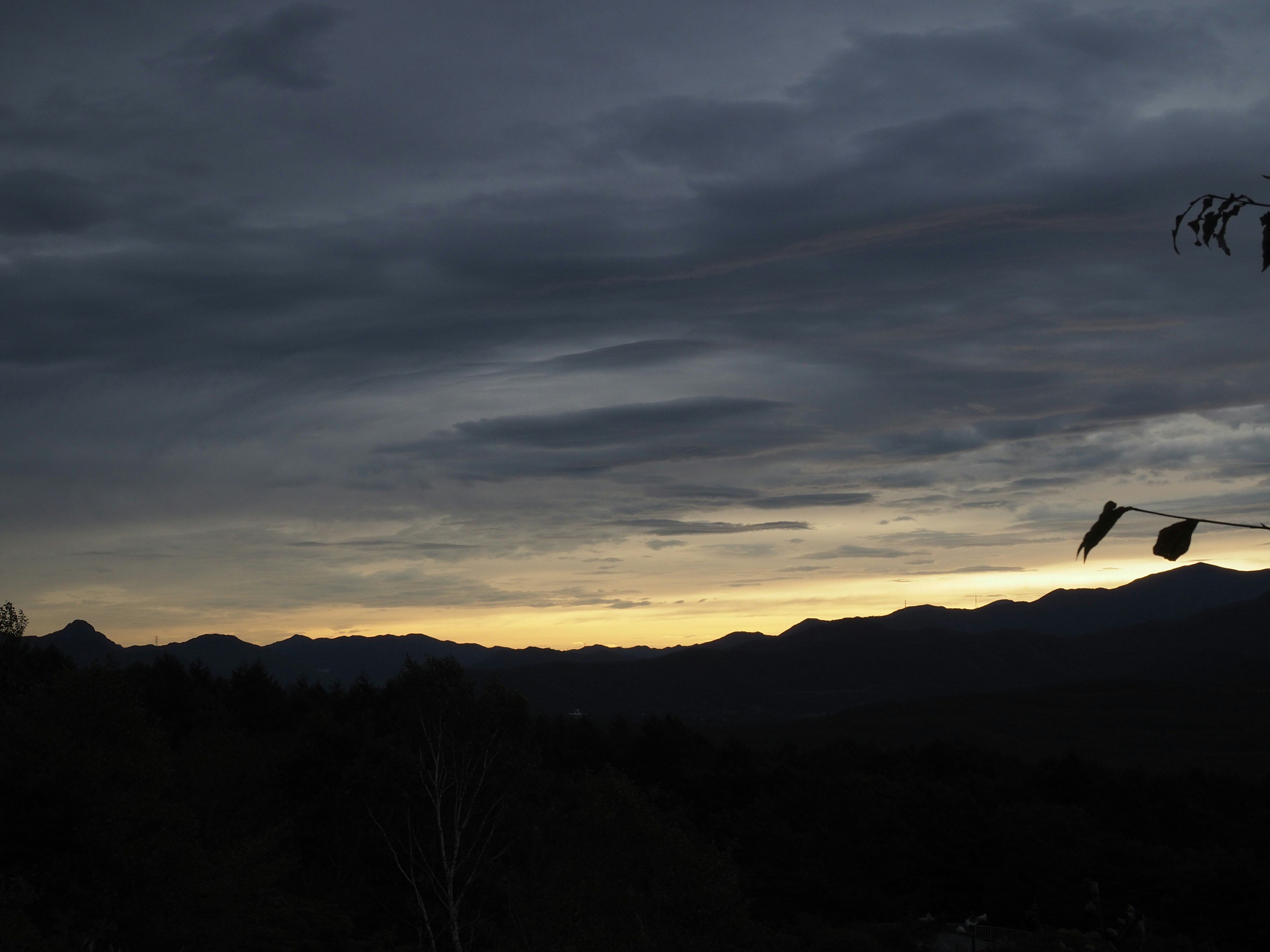 Silhouette de montagnes sous un ciel nuageux sombre avec des teintes de coucher de soleil