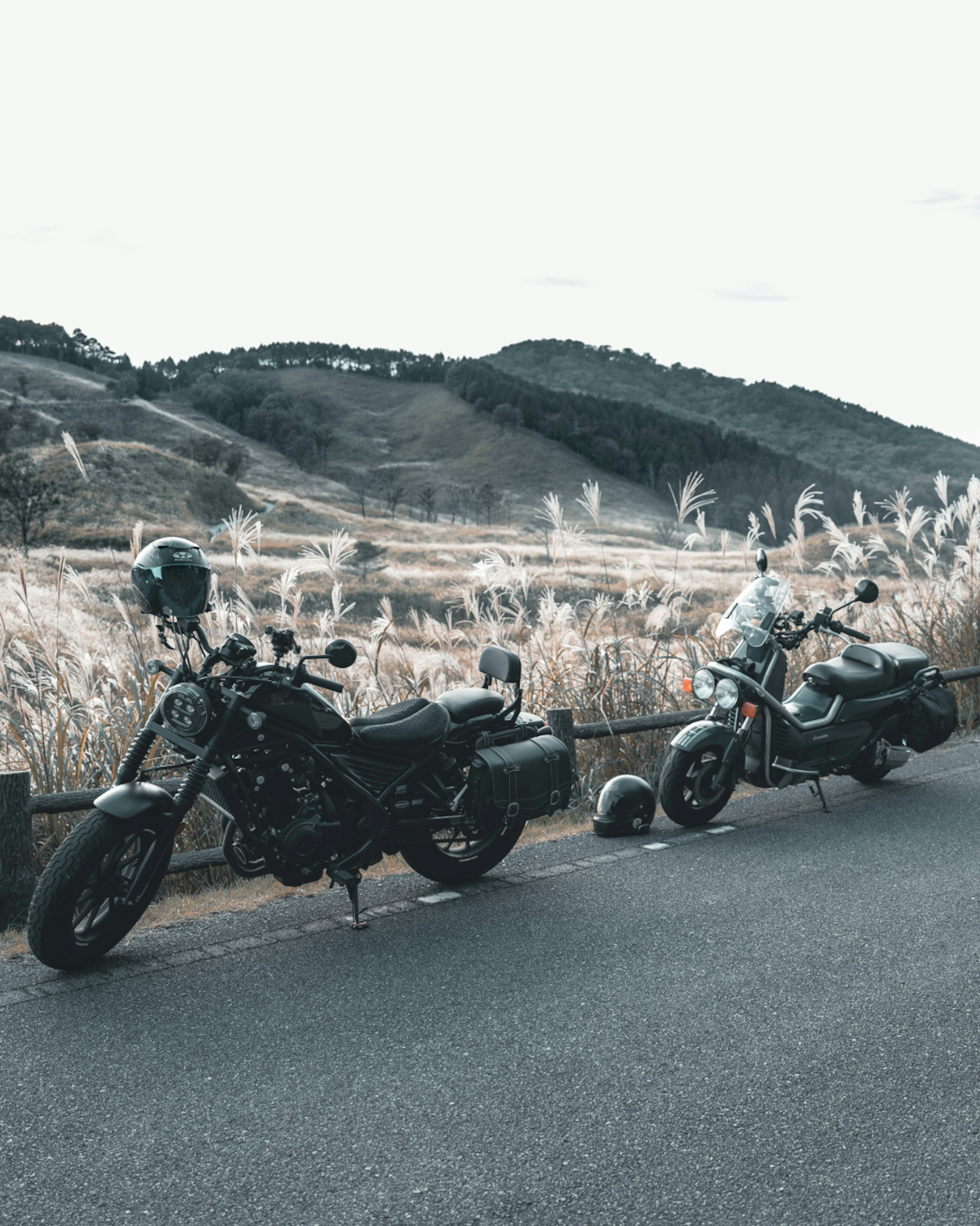 Dos motocicletas estacionadas una al lado de la otra con colinas y praderas al fondo