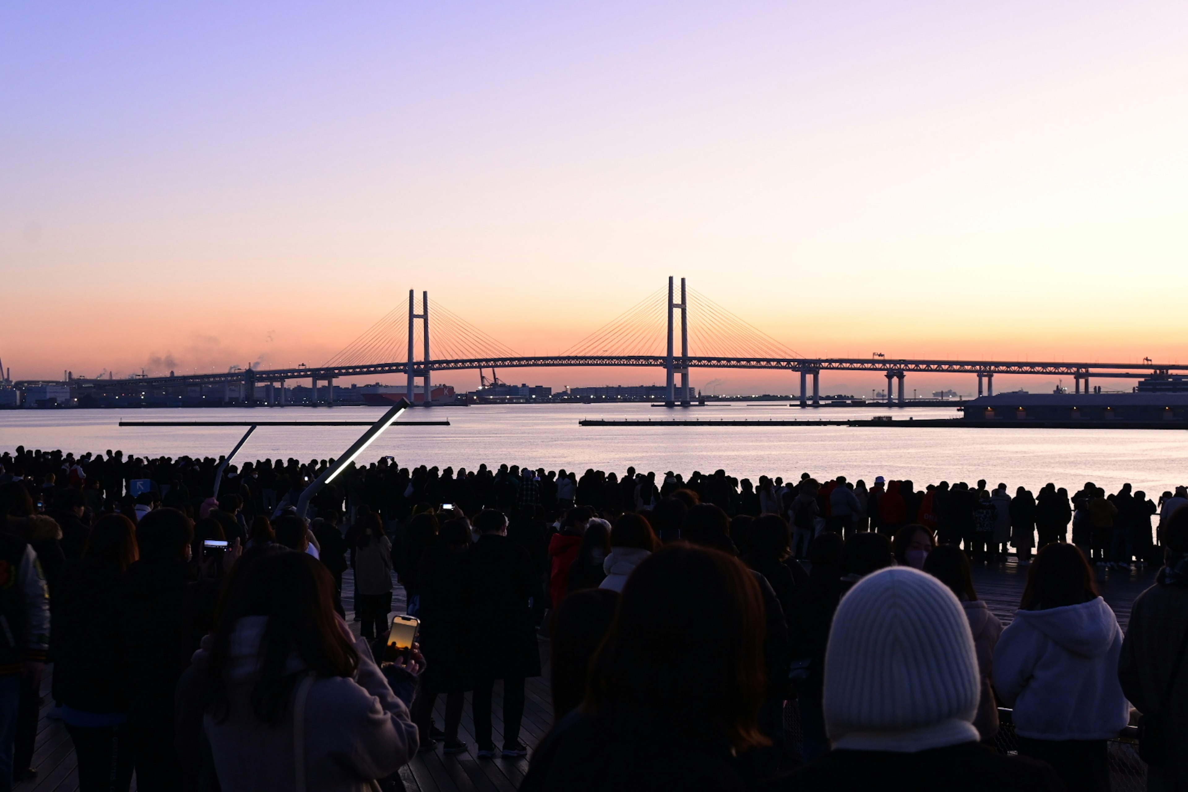 Menschenmenge, die den Sonnenuntergang hinter der Yokohama-Buchtbrücke beobachtet