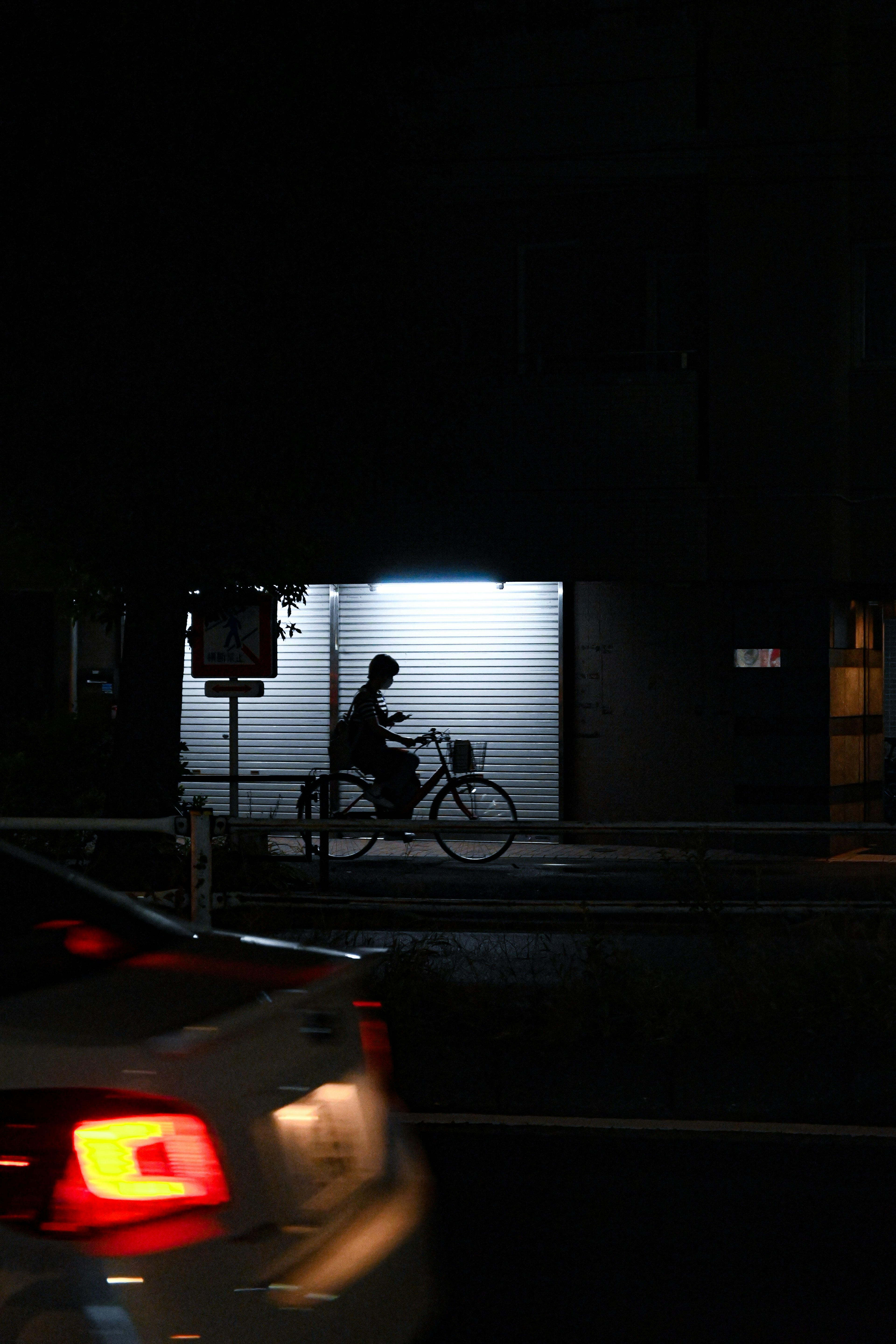 Silhouette di una persona in bicicletta in una strada buia con un muro luminoso