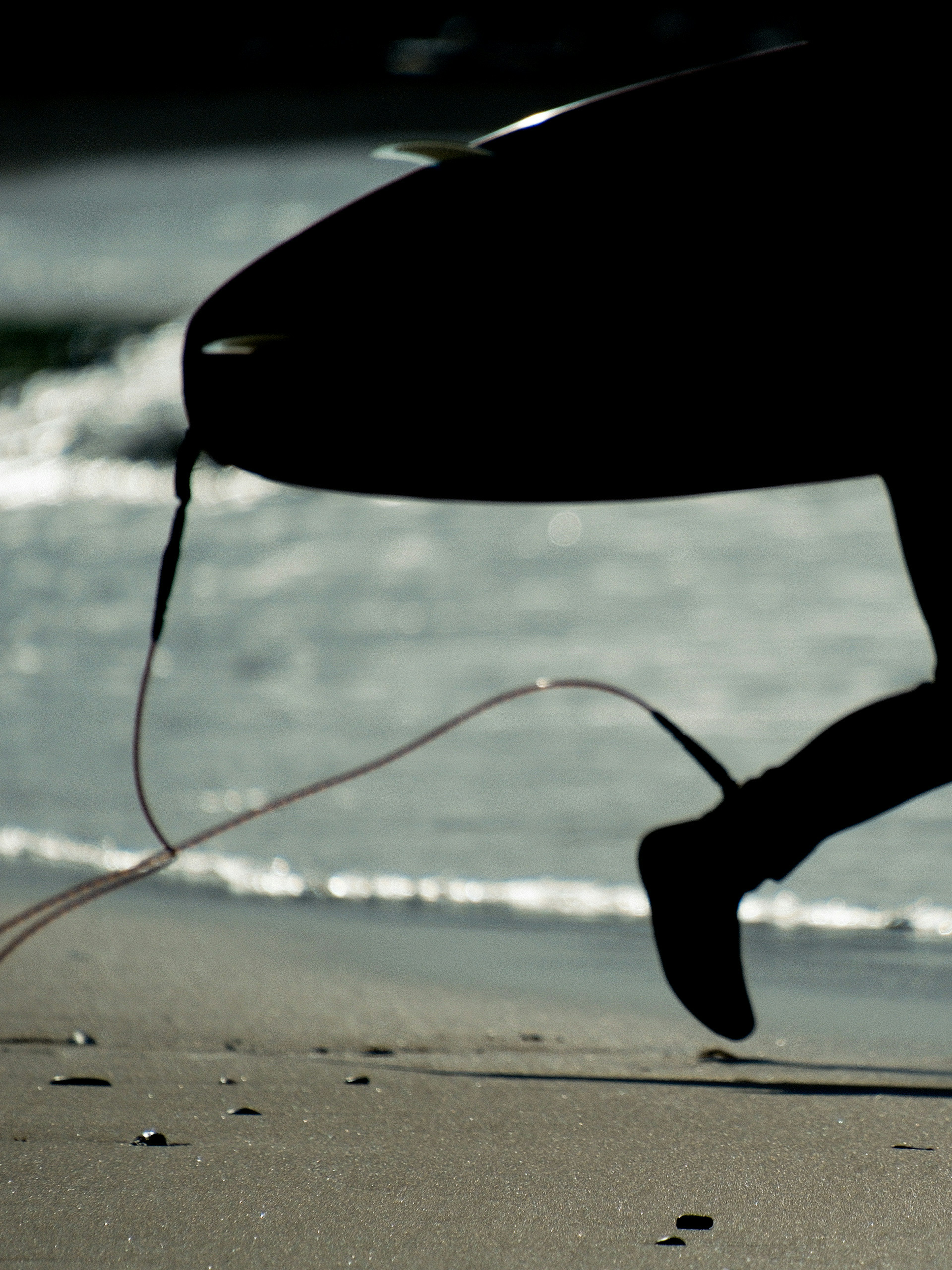 Silhouette of a surfer running on the beach holding a surfboard with waves in the background