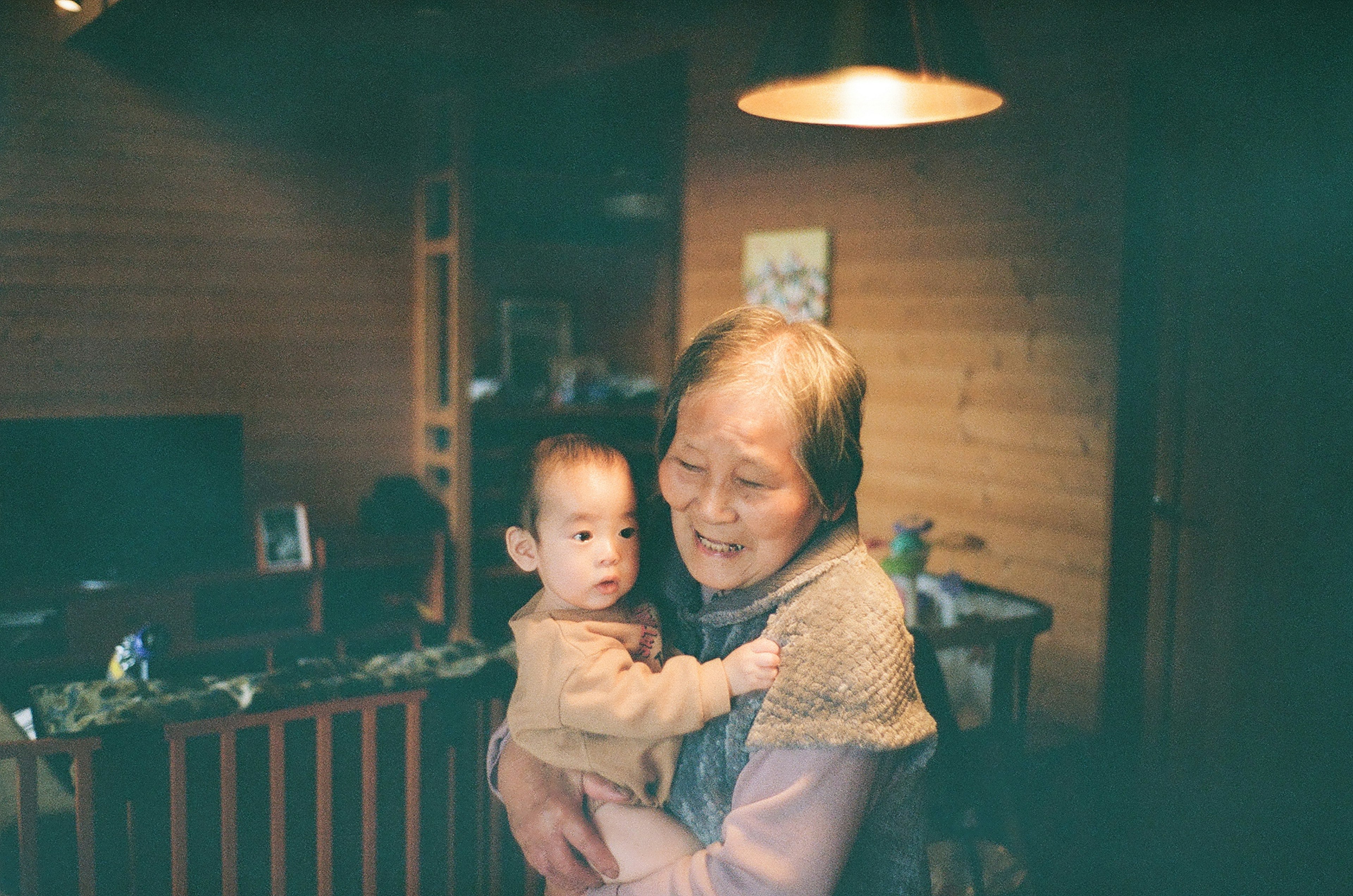 A grandmother smiling while holding a baby in a cozy indoor setting