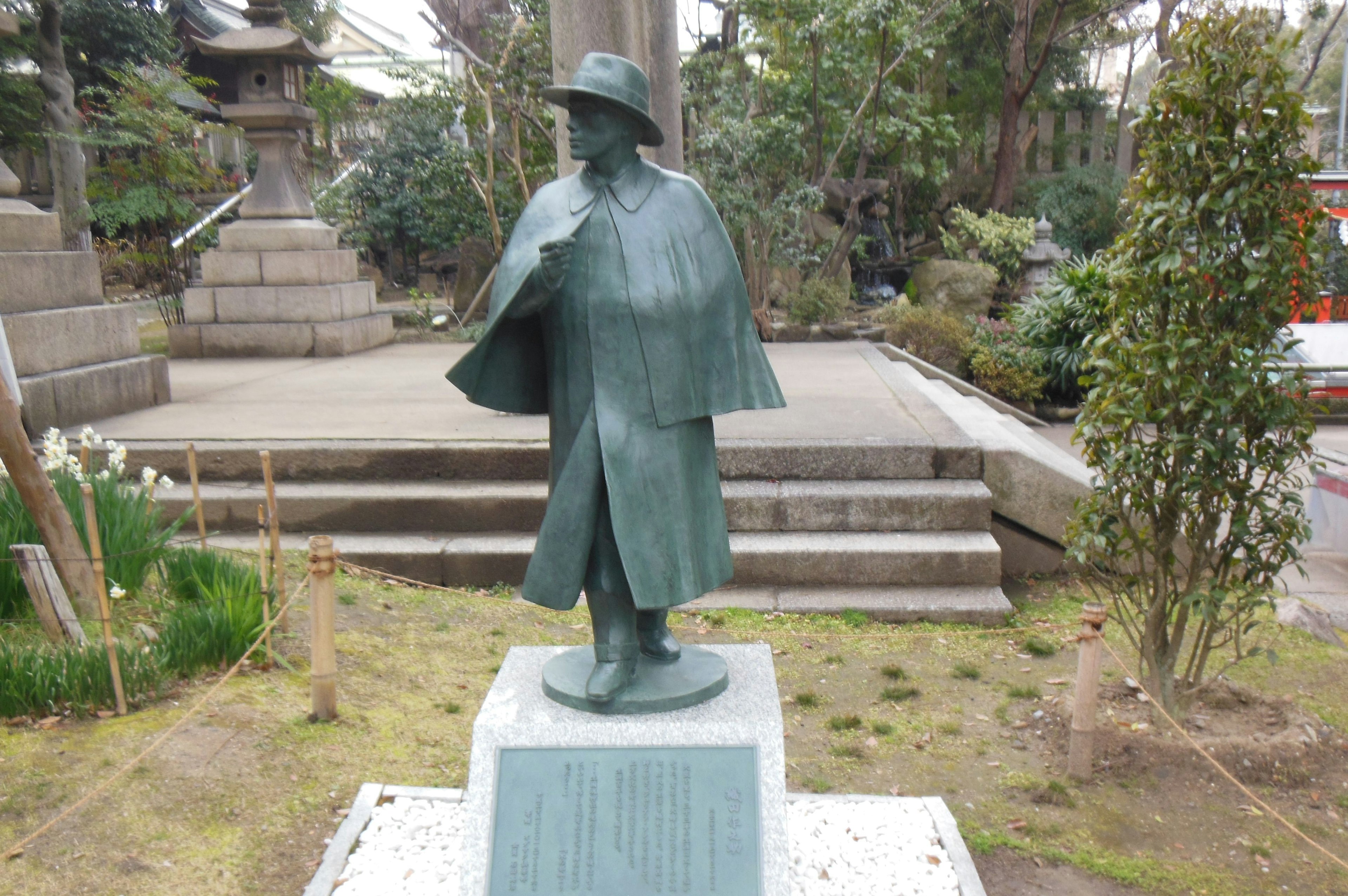 Statua in bronzo di una persona con un cappello che si erge in un giardino