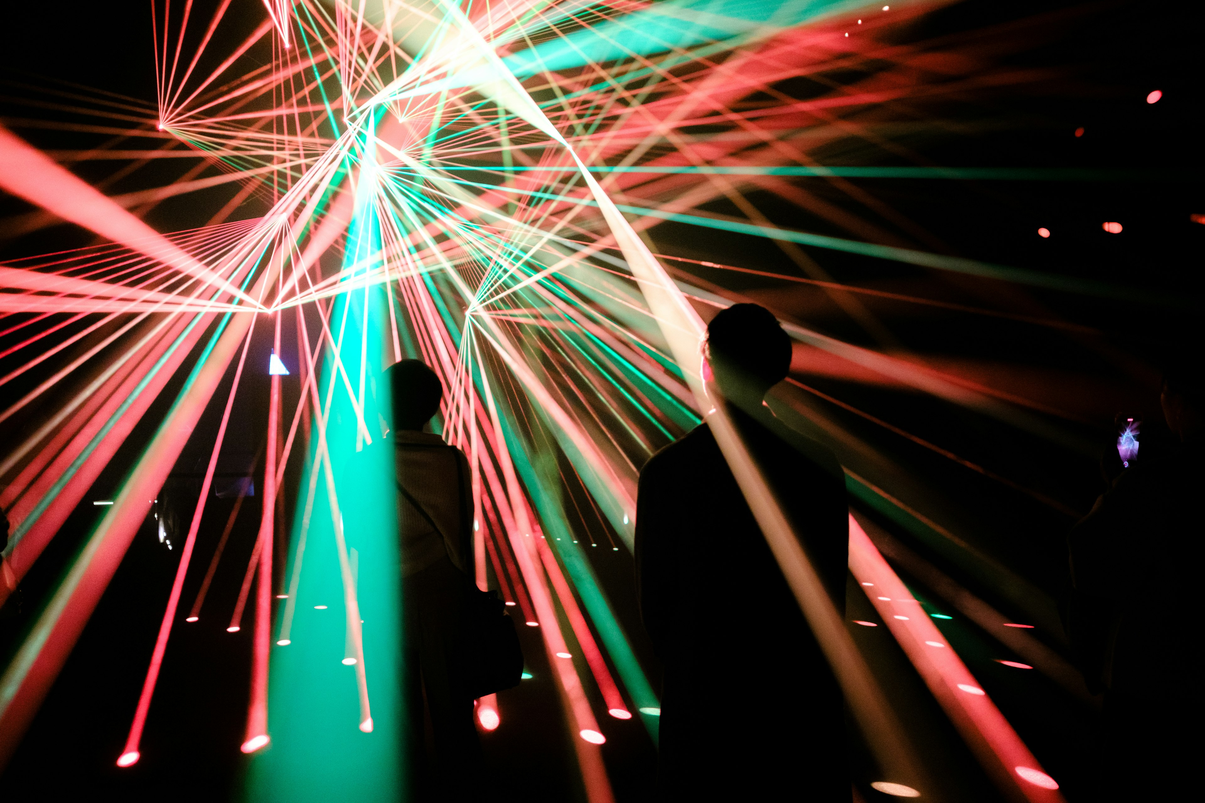 People standing amidst intersecting colorful laser beams