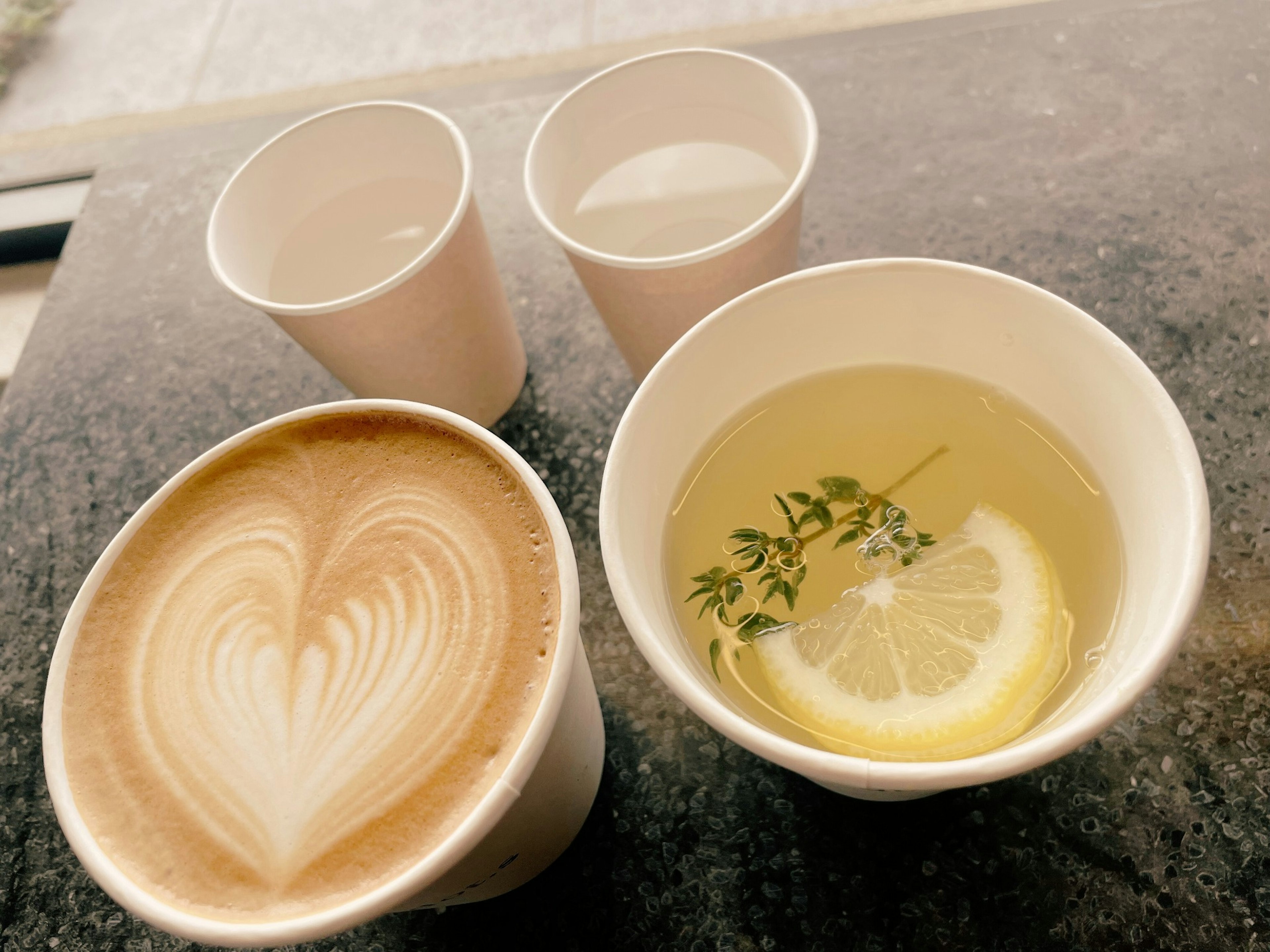 Ein Latte mit Herz-Latte-Art und eine Tasse Kräutertee mit Zitrone und Kräutern