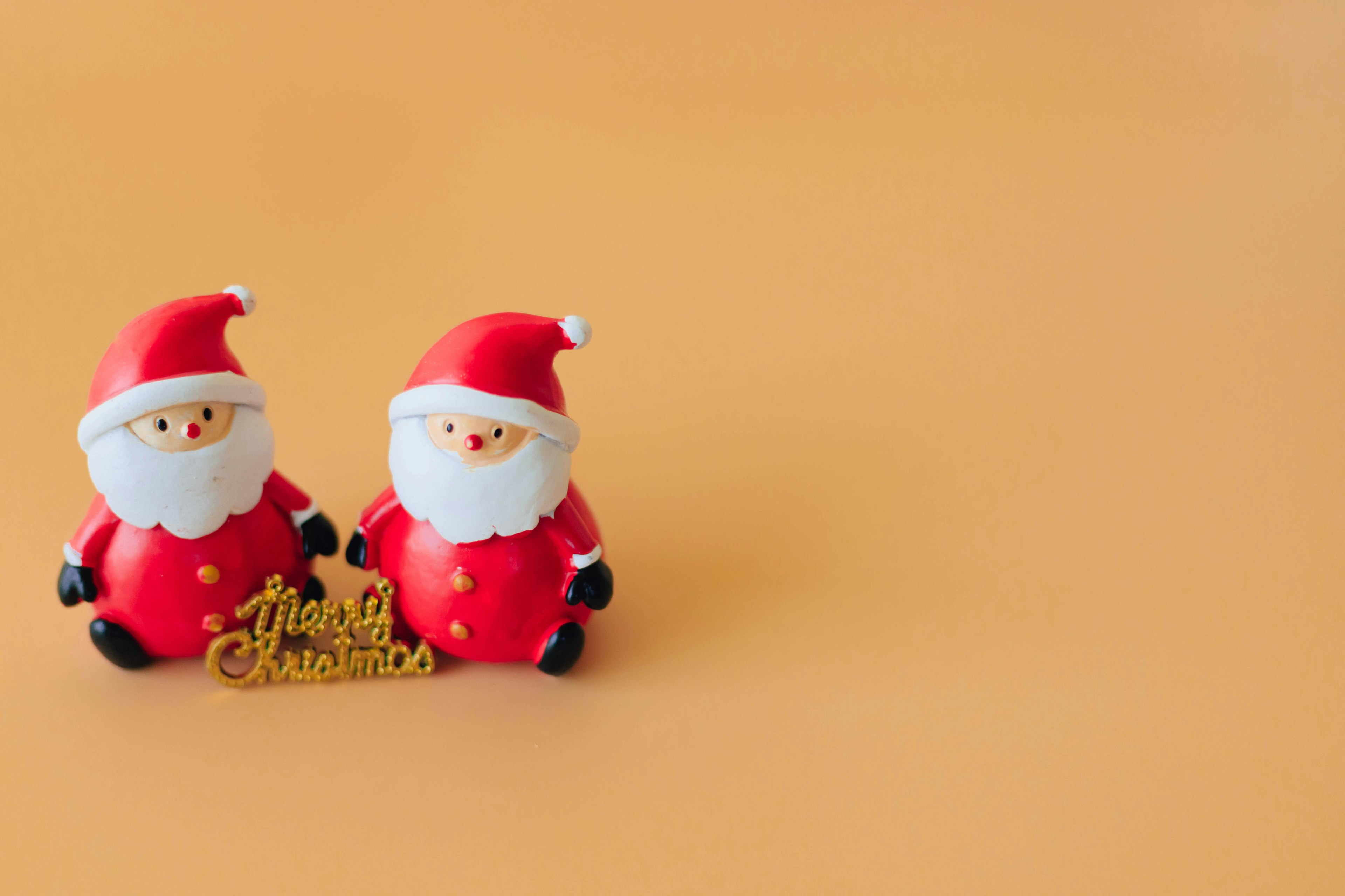 Dos figuritas de Santa Claus con trajes rojos y un cartel de Feliz Navidad