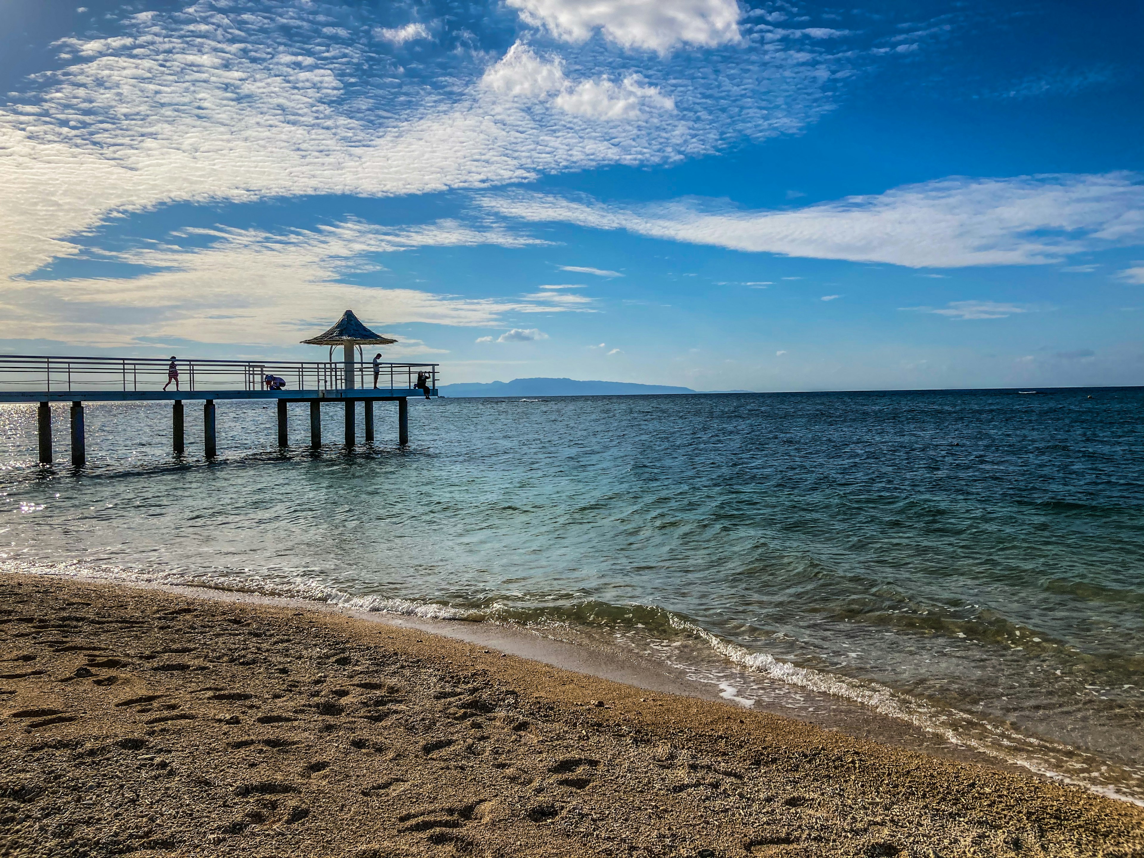 Escena de playa con un muelle bajo un cielo azul con nubes dispersas