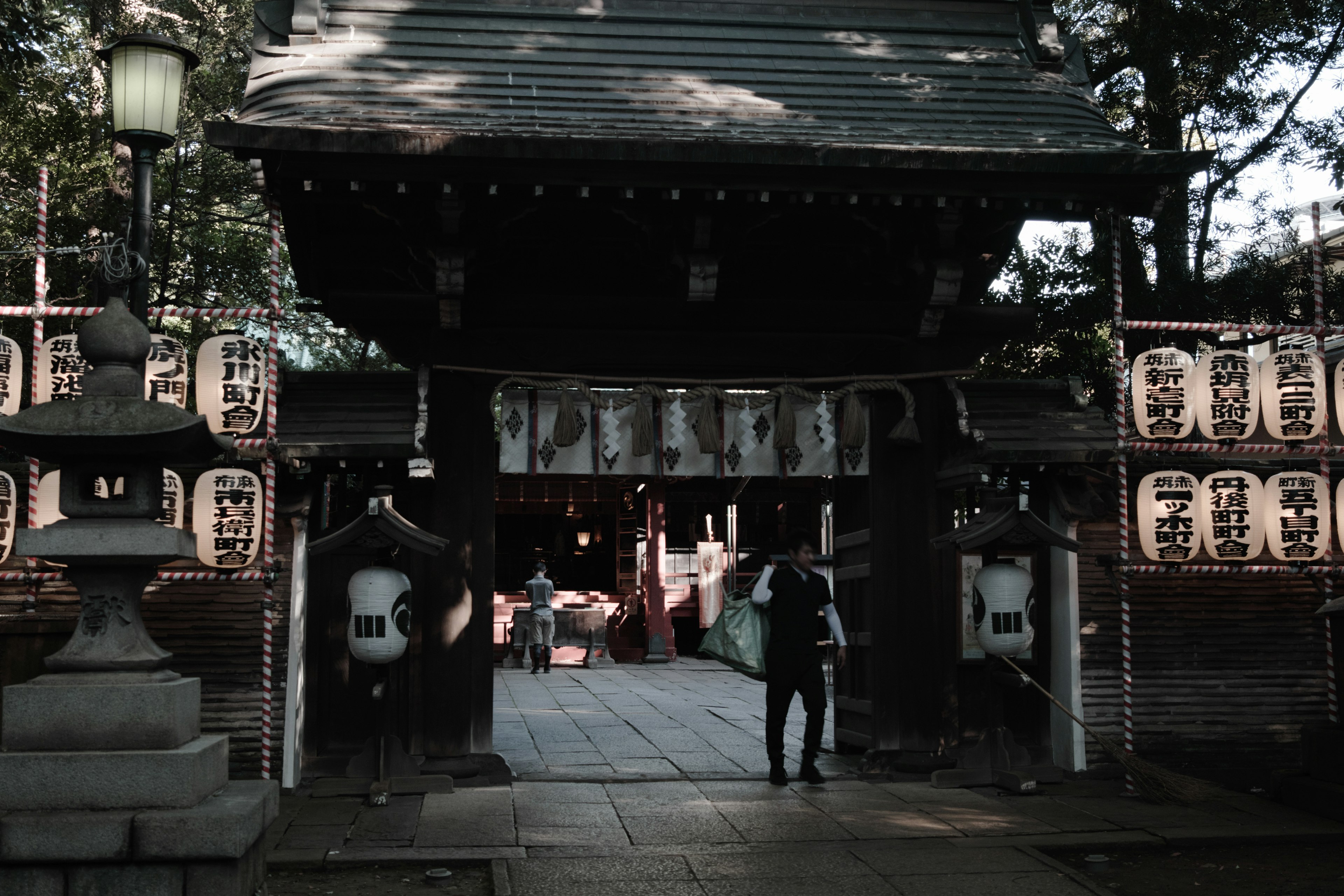 Eingang eines traditionellen japanischen Schreins mit Laternen und dekorativer Tür mit einem Besucher