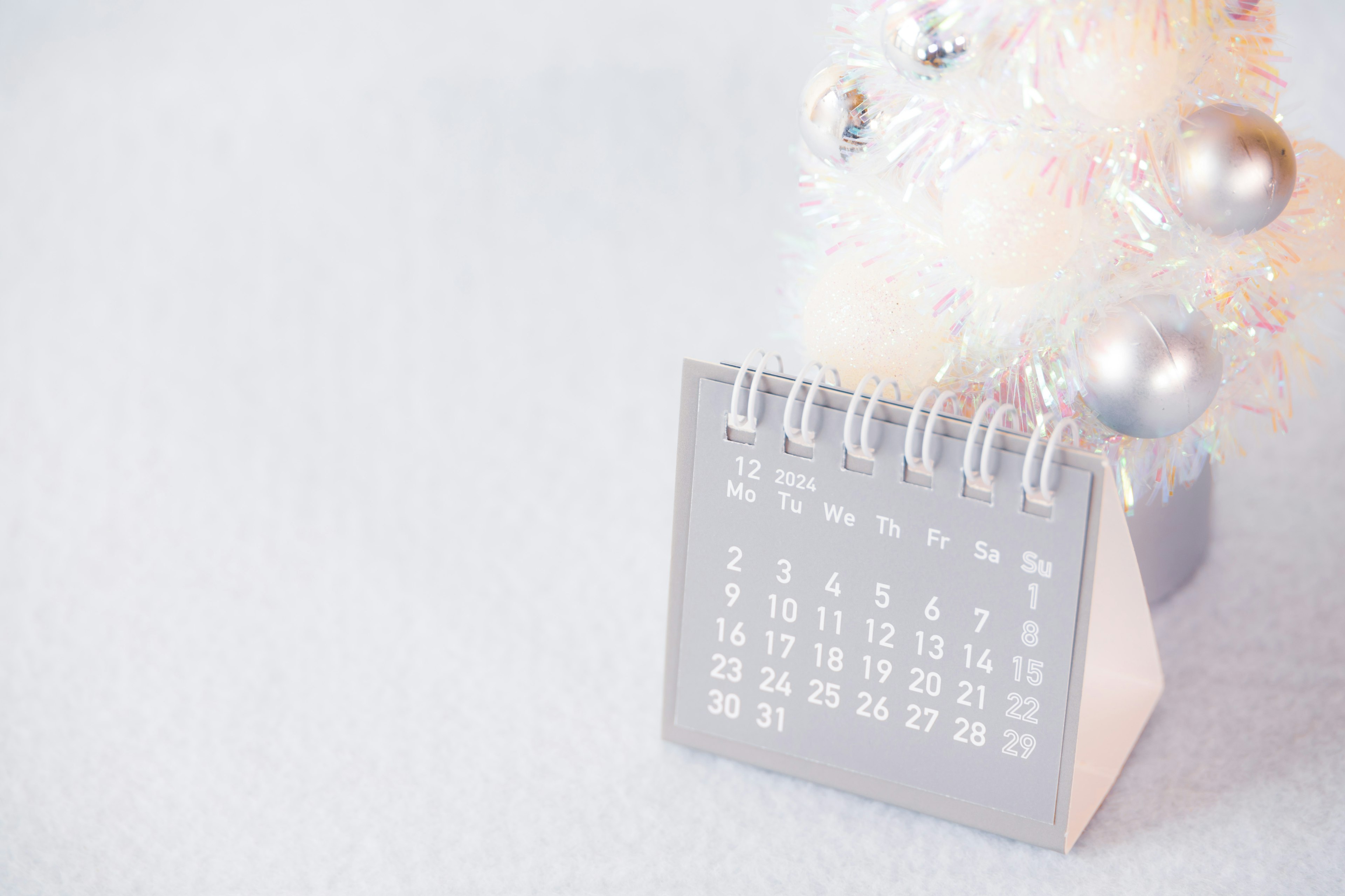 A calendar beside a white Christmas tree with silver ornaments