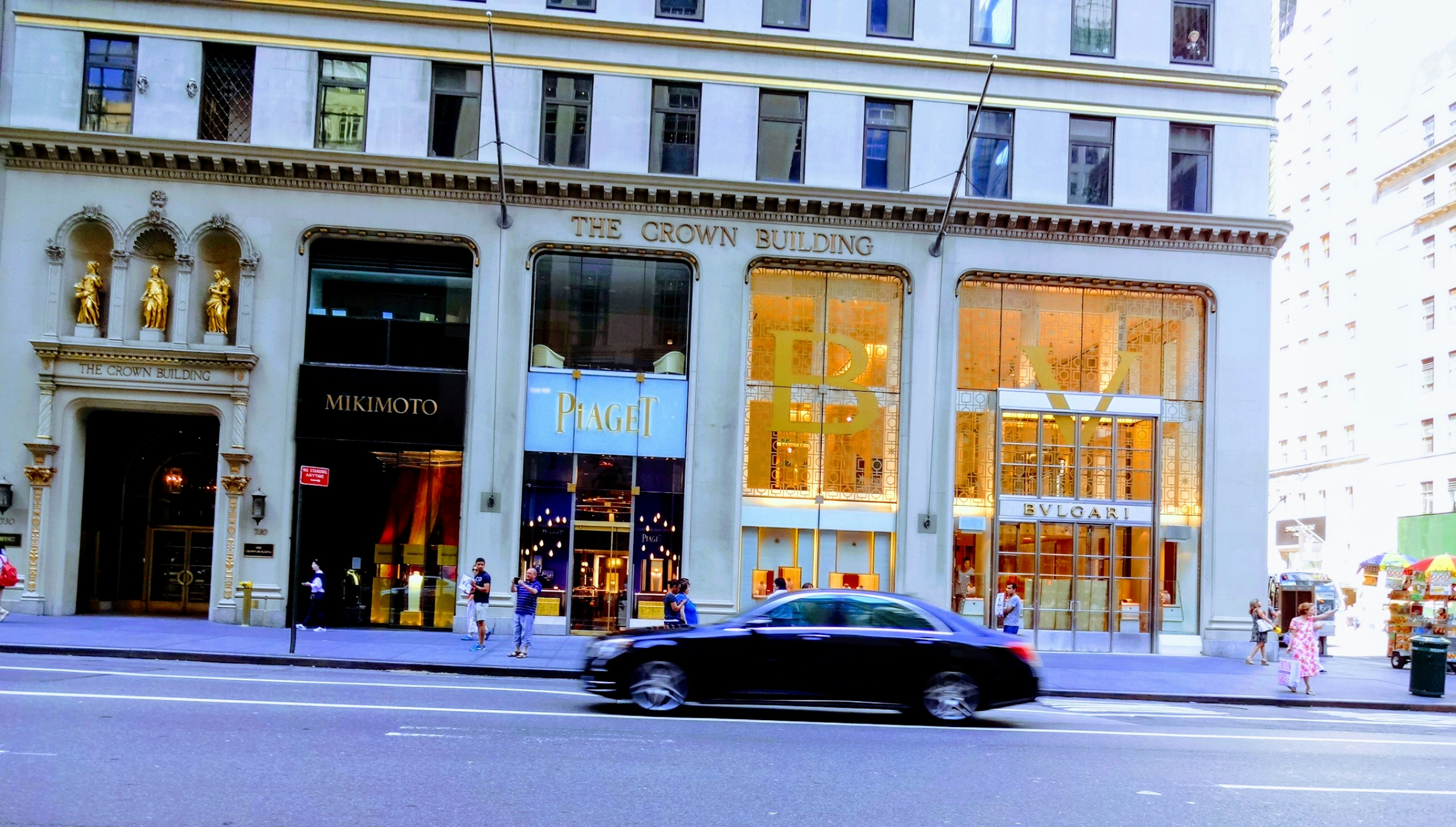 Facade of a luxury store in the city corner with a black car passing by