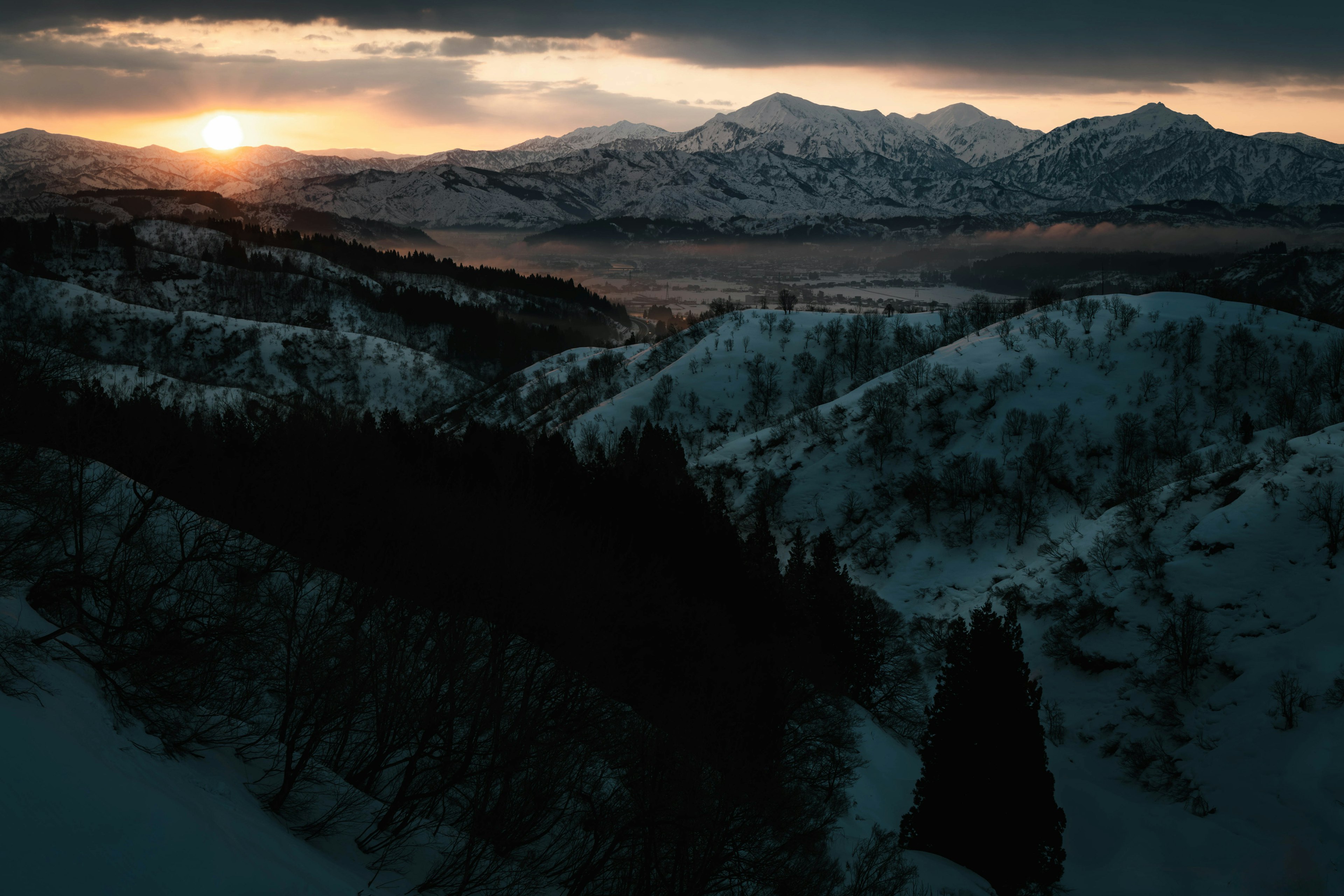 Schneebedeckte Berge mit Tälern und einem Sonnenuntergang im Hintergrund