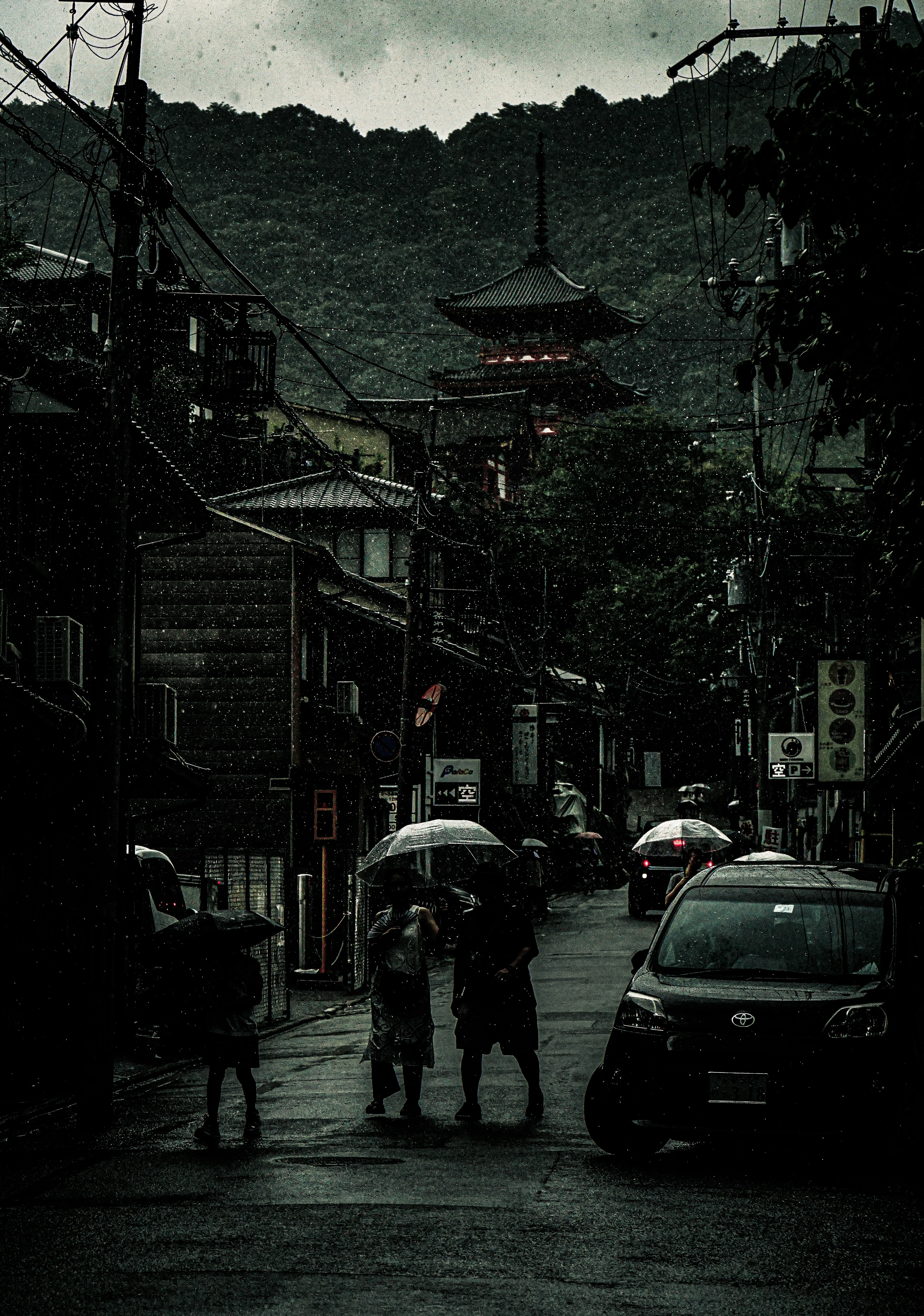 雨の中を傘をさして歩く人々と暗い街並みの風景