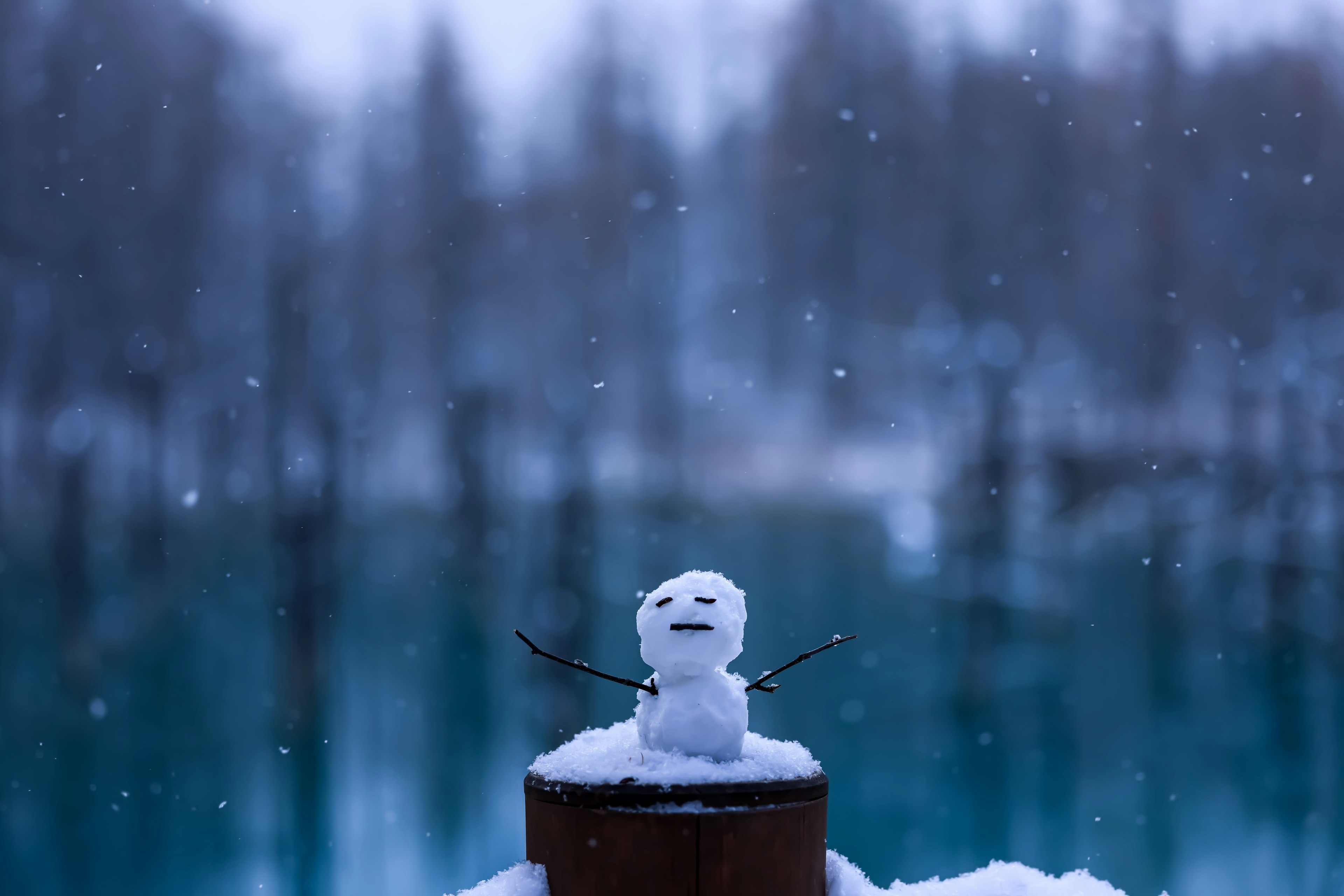 Kleiner Schneemann steht im Schnee mit blauem Wasserhintergrund