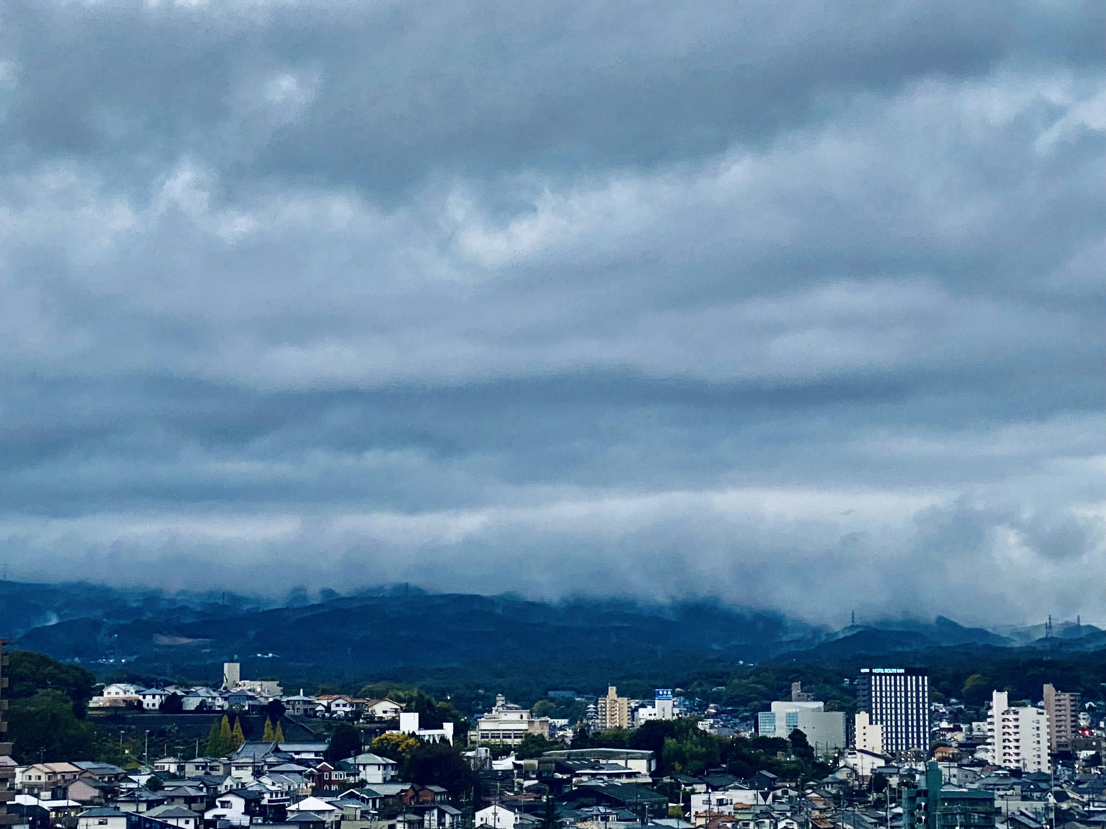 Pemandangan kota di bawah langit biru dengan siluet pegunungan