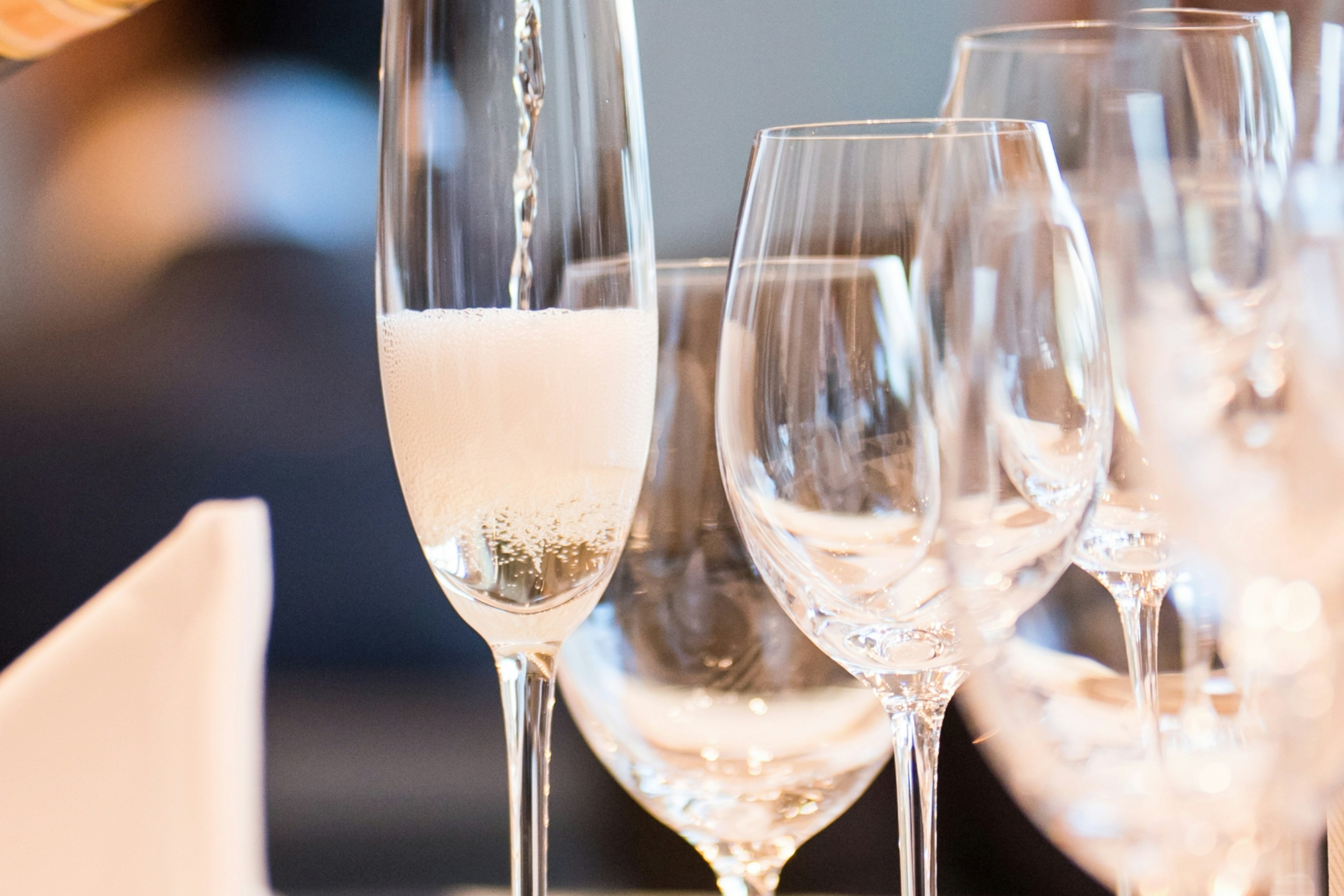 Einschenken eines sprudelnden Getränks in ein Champagnerglas mit anderen Gläsern im Hintergrund