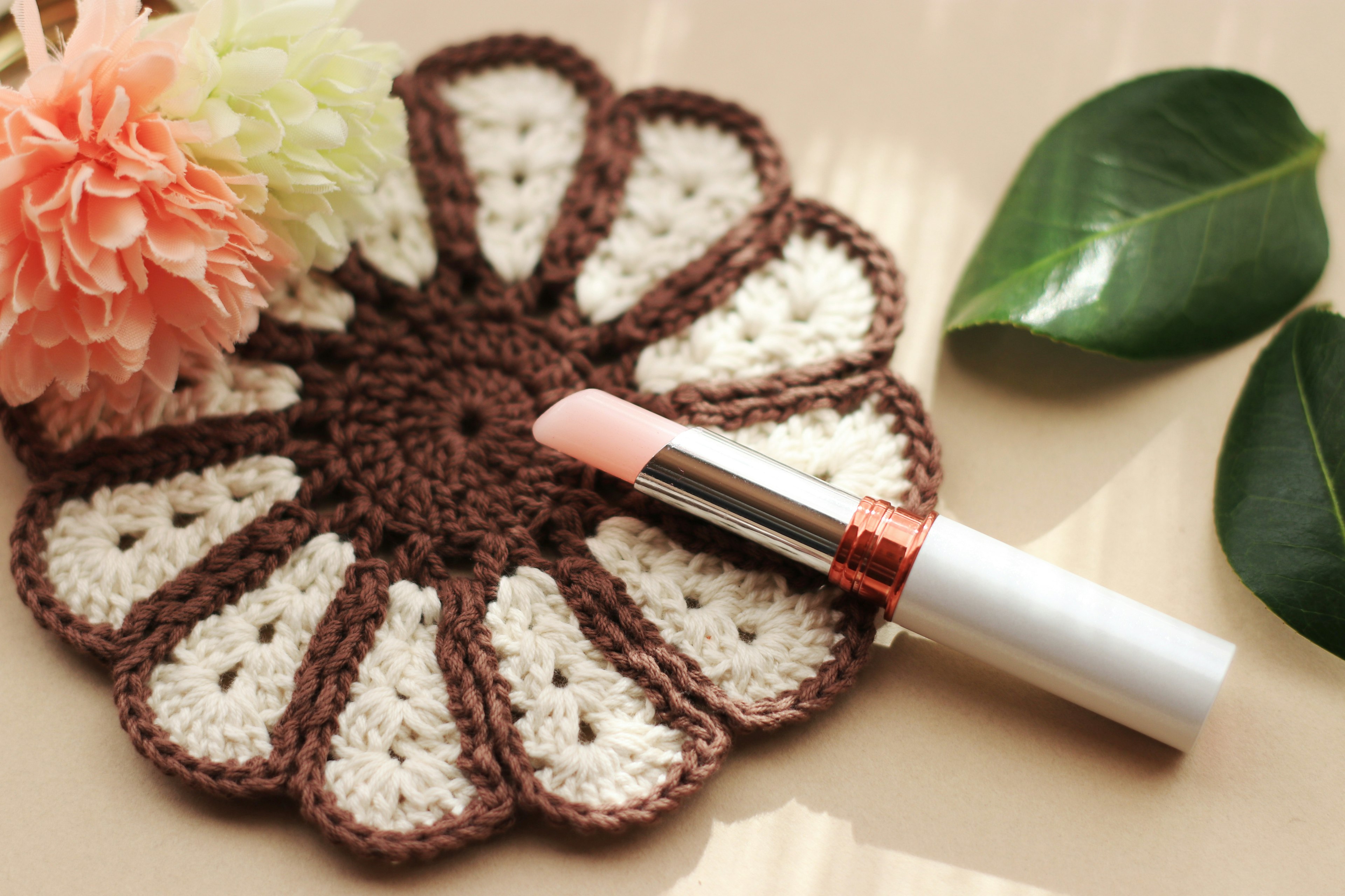 A pale pink lipstick placed on a flower-shaped coaster with a floral arrangement