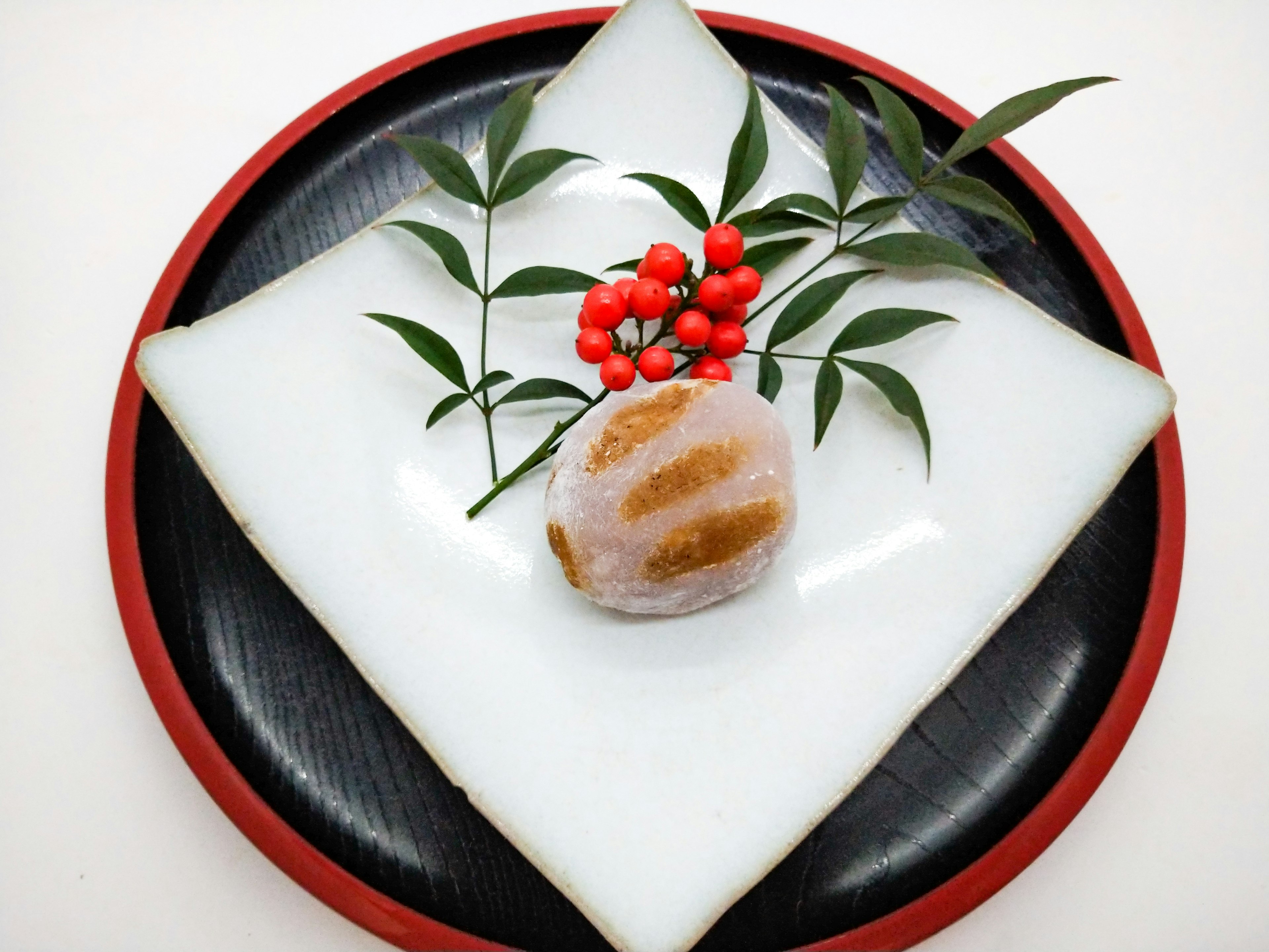 Traditional Japanese sweets arranged on a white plate with red berries and green leaves