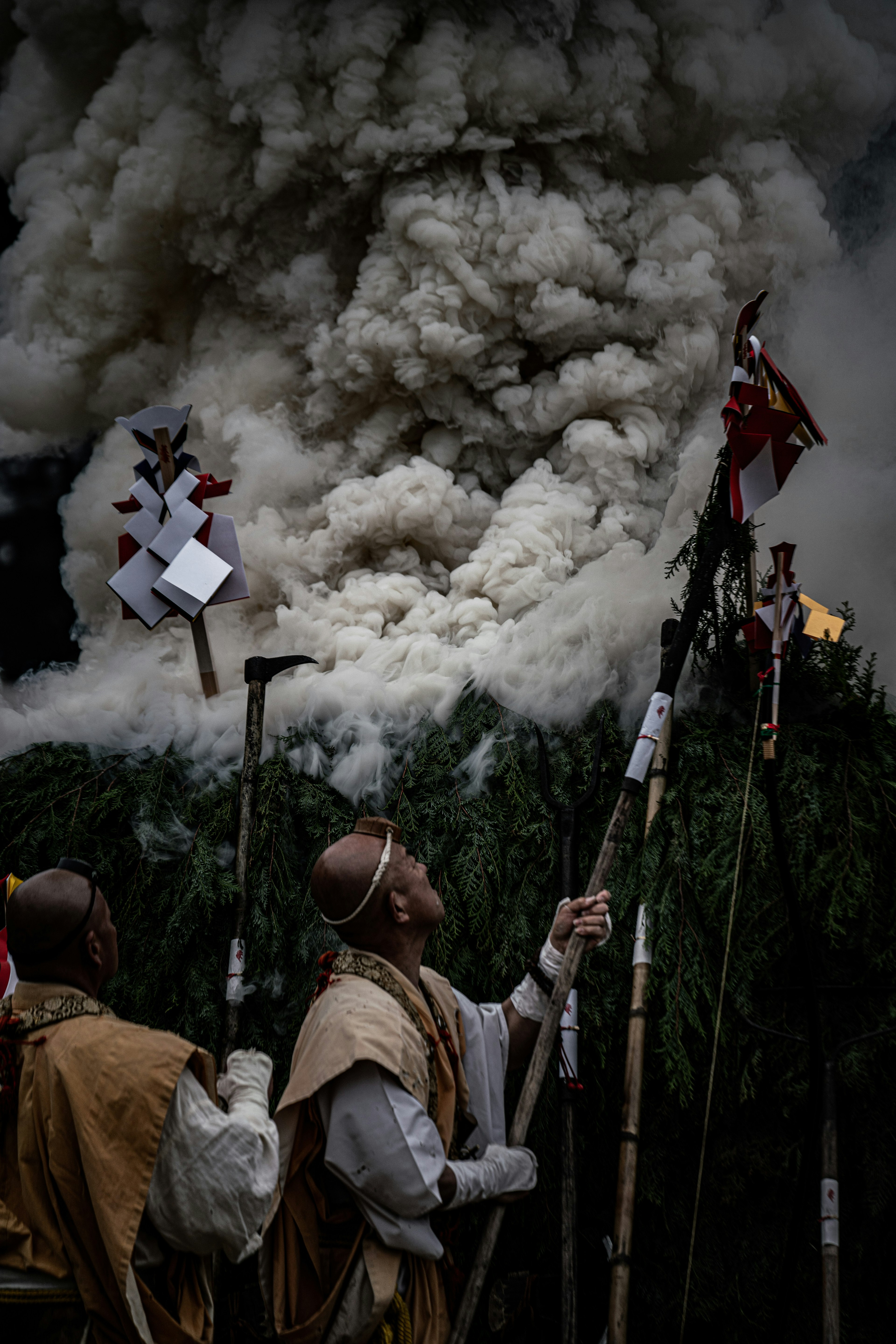 Escena de festival con humo y personas en atuendos tradicionales sosteniendo palos