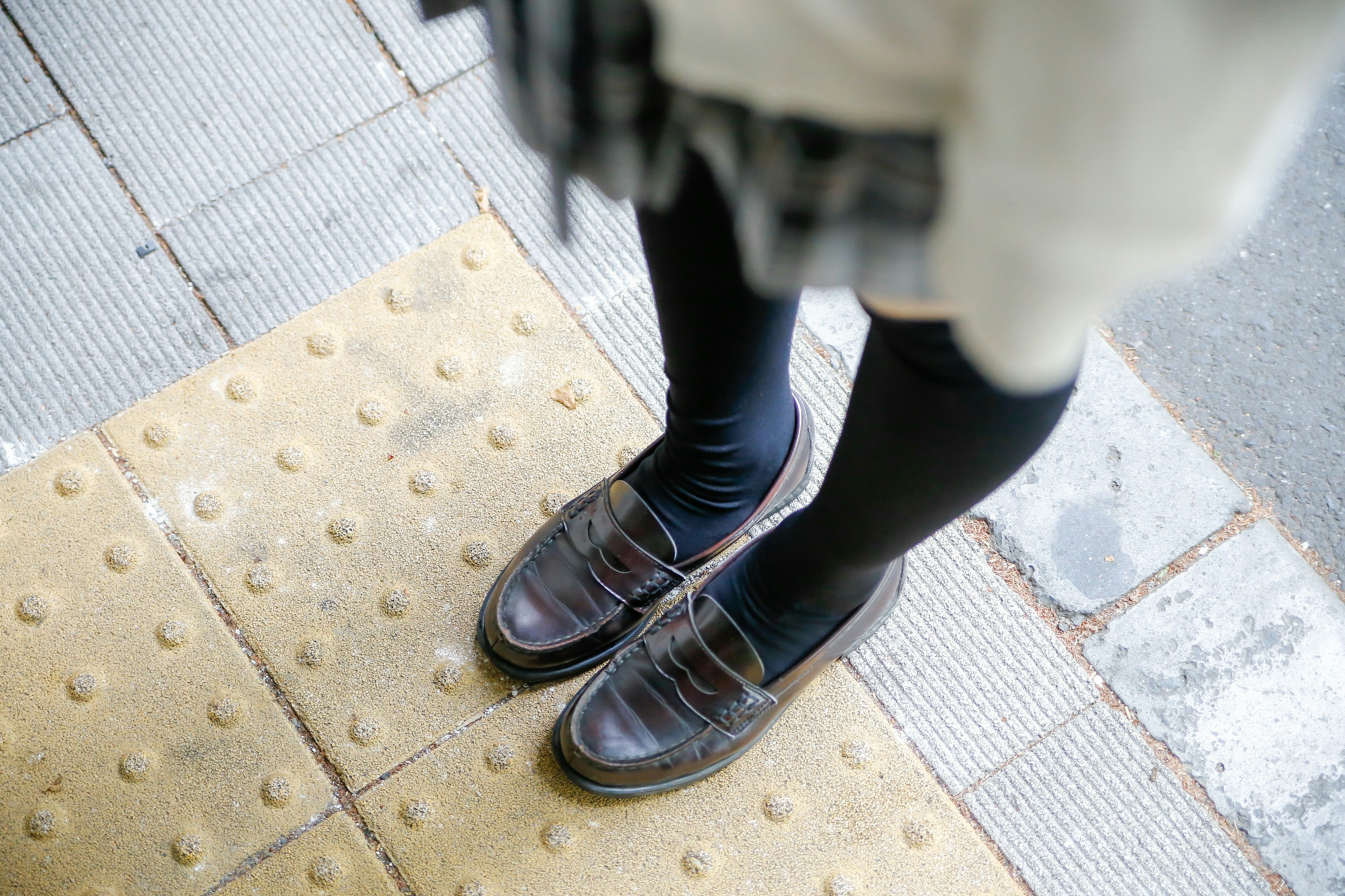 Close-up of feet in brown shoes and black tights on a textured pavement