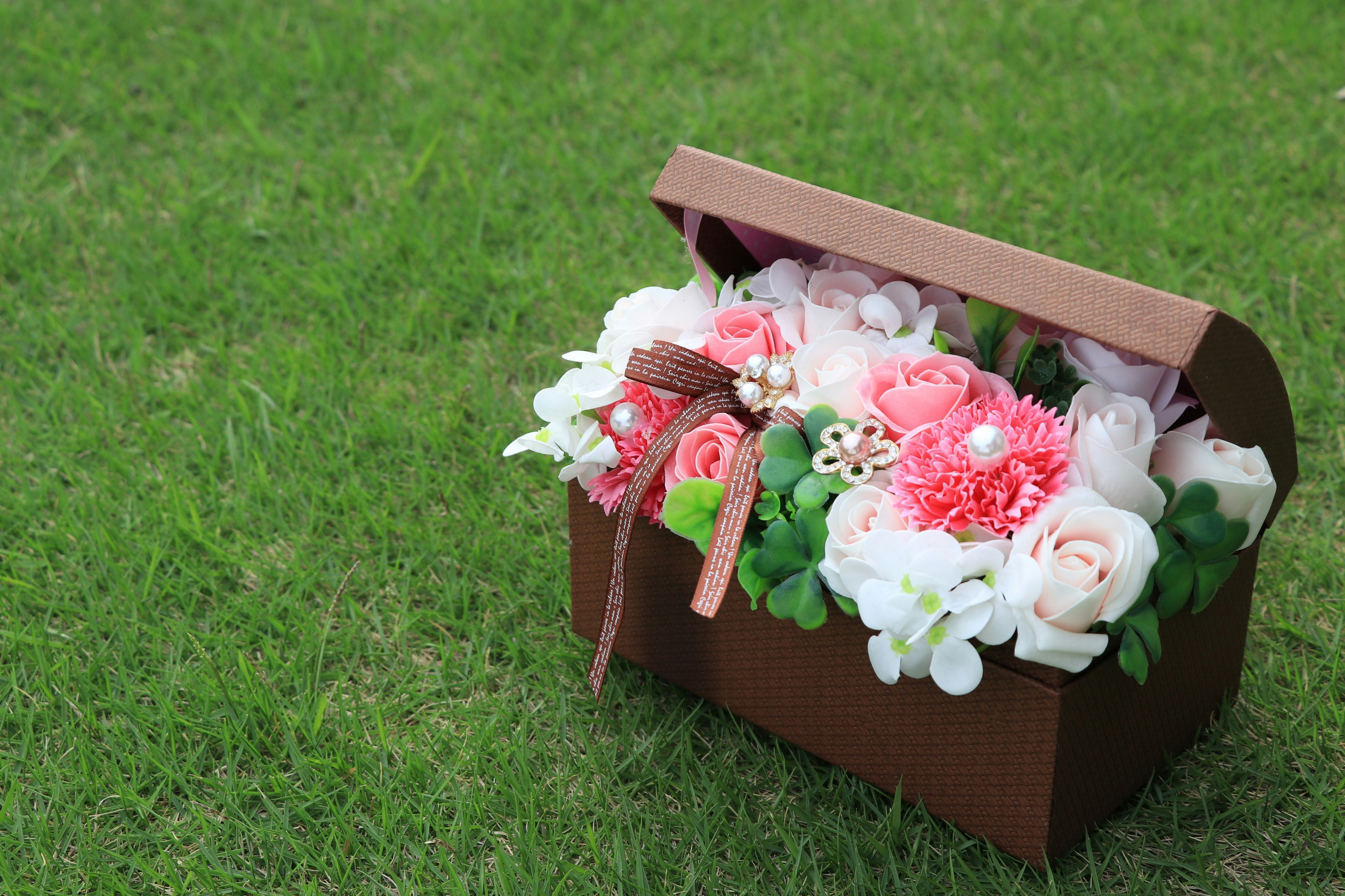 Une boîte brune remplie de fleurs roses et blanches posée sur de l'herbe verte